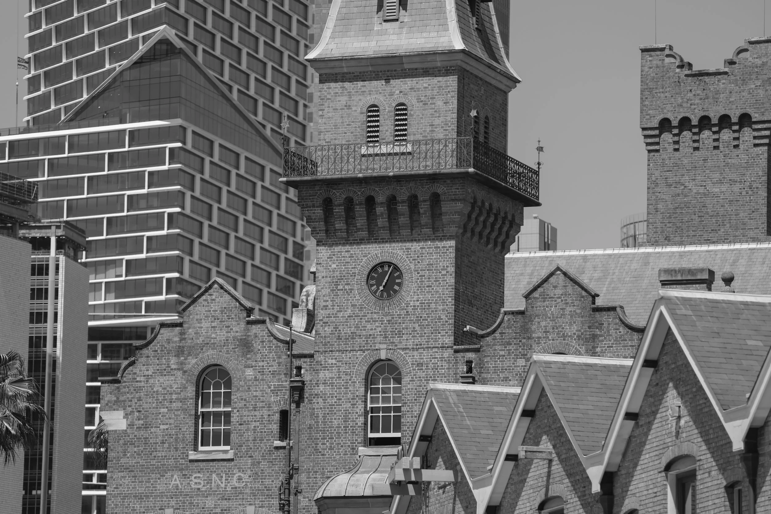 Black and white photo of a historic brick church with a clock tower, surrounded by modern high-rise buildings.