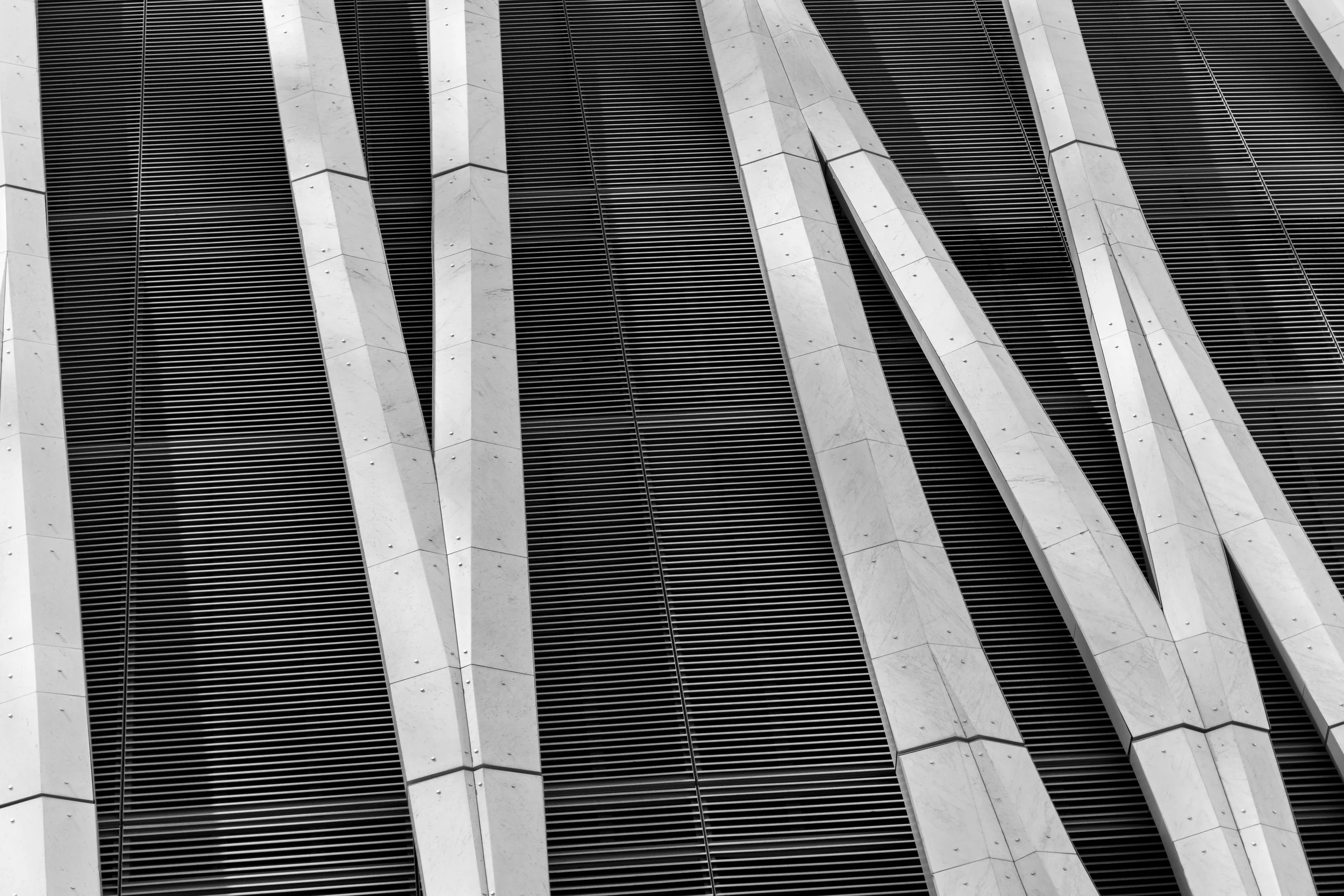 Close-up photograph of a modern building facade with vertical white concrete beams and black horizontal louvers.