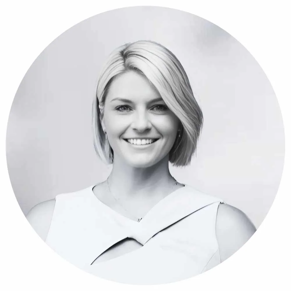 Black and white portrait of a smiling woman with short blonde hair, wearing a sleeveless top with an asymmetrical neckline.