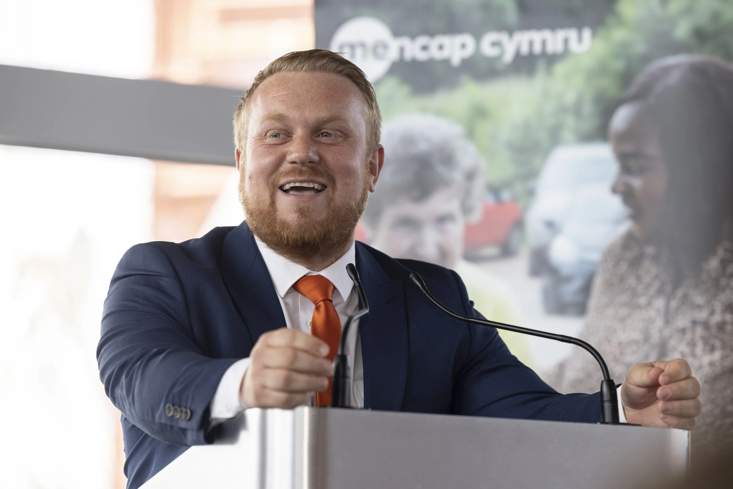 Rob Osborne delivering a keynote at a conference, speaking confidently at the podium with a microphone.