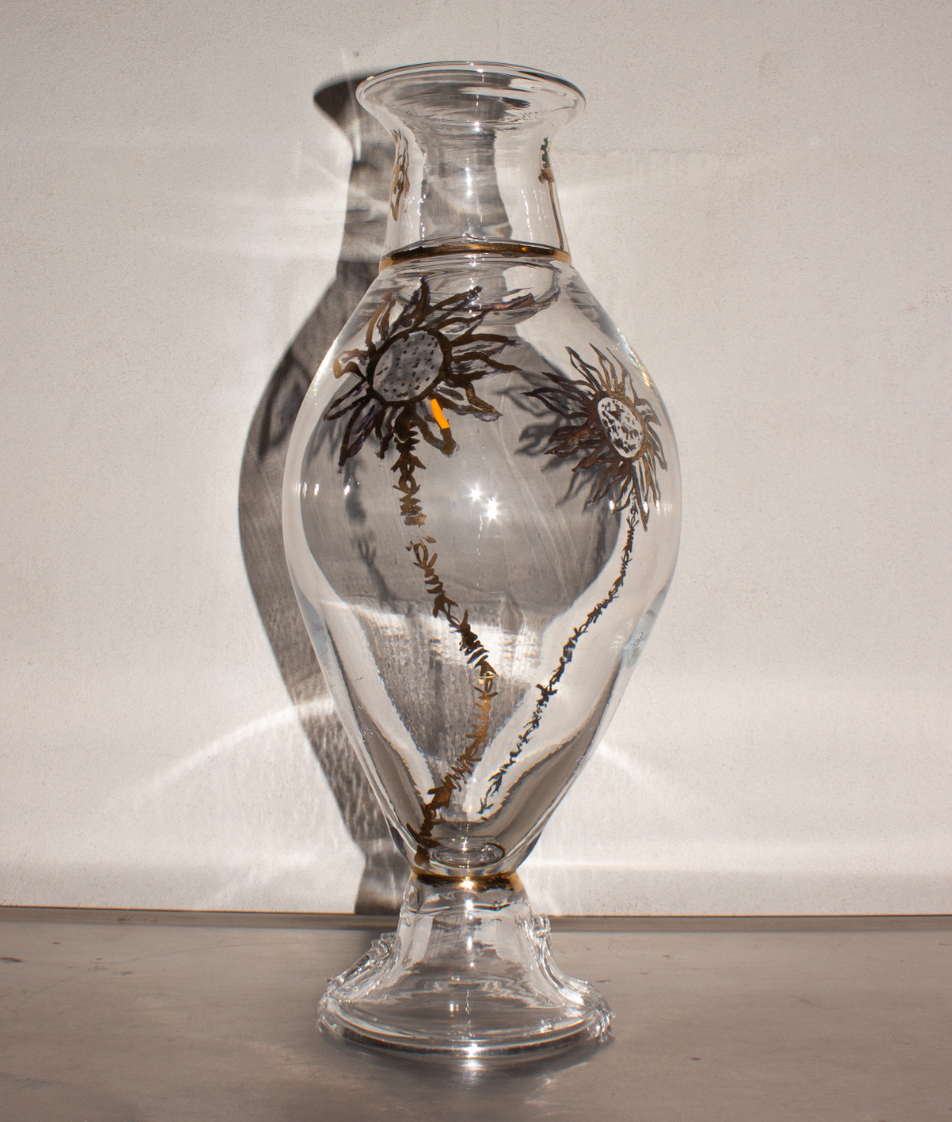 A clear glass vase with floral designs, casting shadows and reflections on the surface and wall behind it.