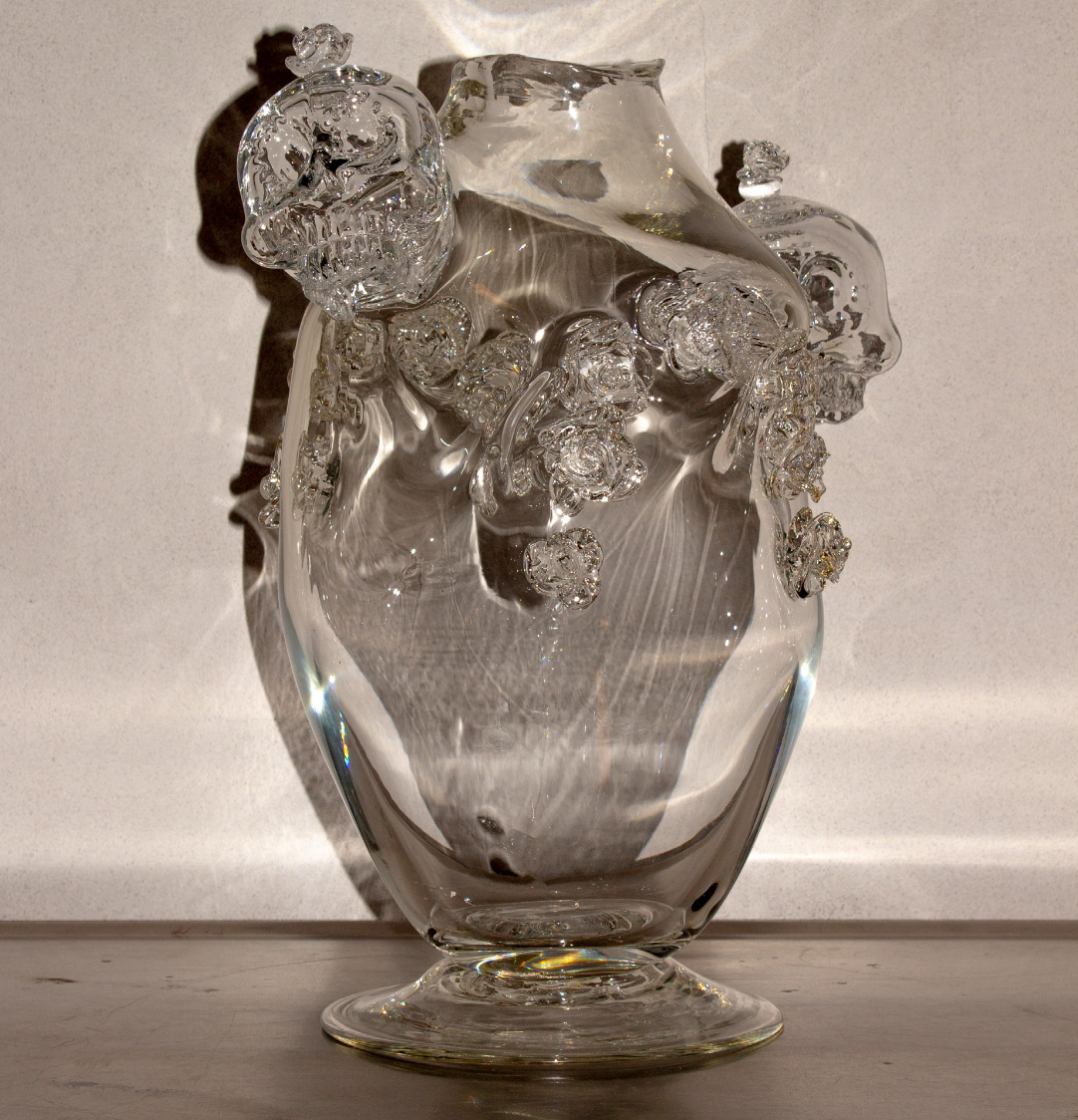 Glass vase with skull and floral designs, transparent and reflective.