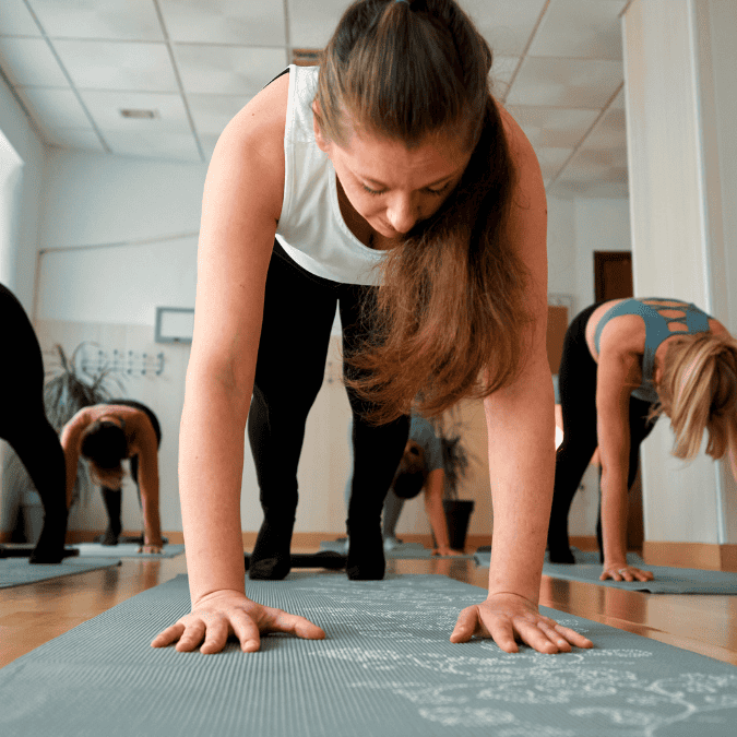 Women participating in a yoga class on mats, with one woman in the foreground doing a plank pose.