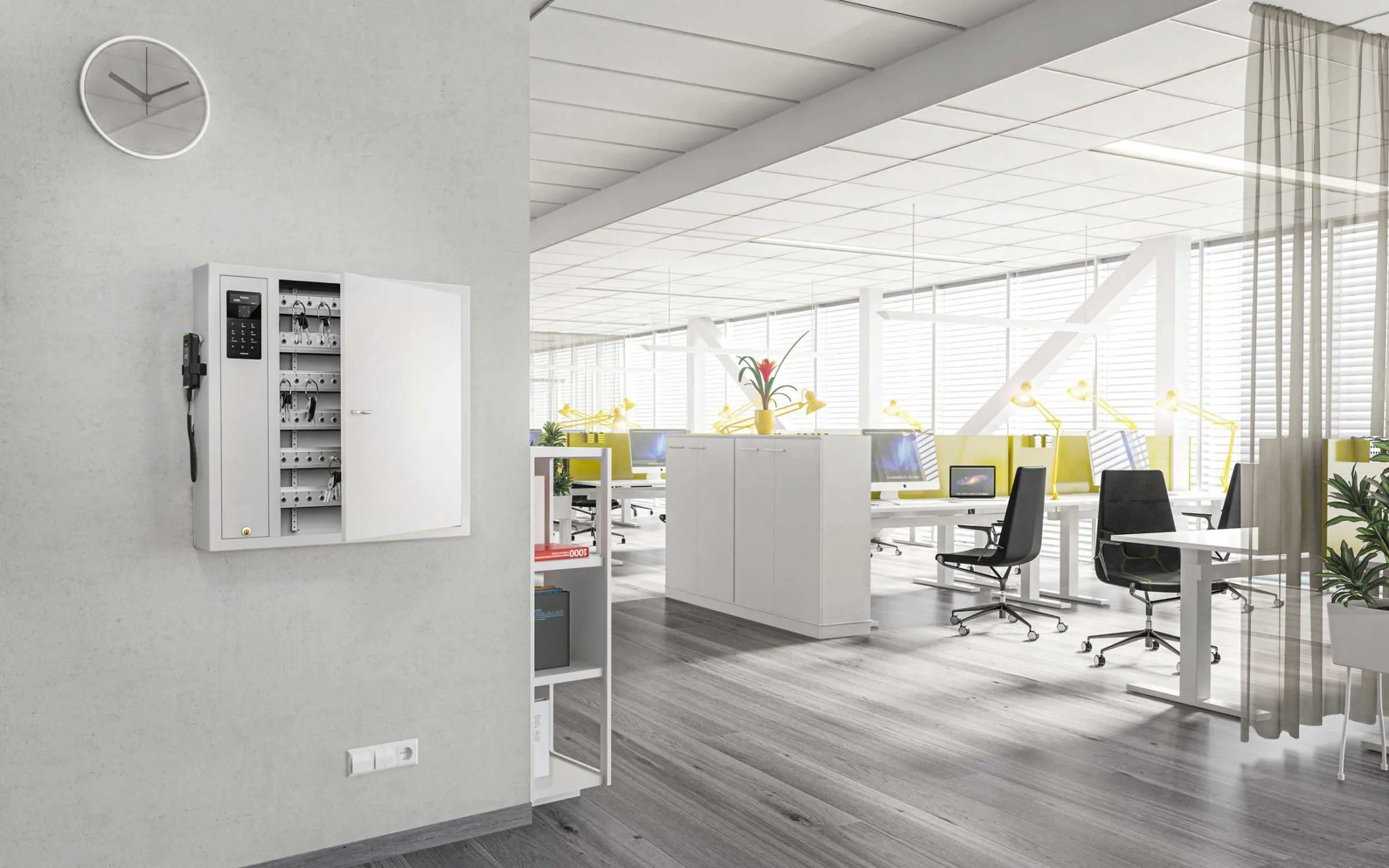 Bright modern open-plan office with desks, computer monitors, black office chairs, plants, large windows, and a wall-mounted equipment cabinet