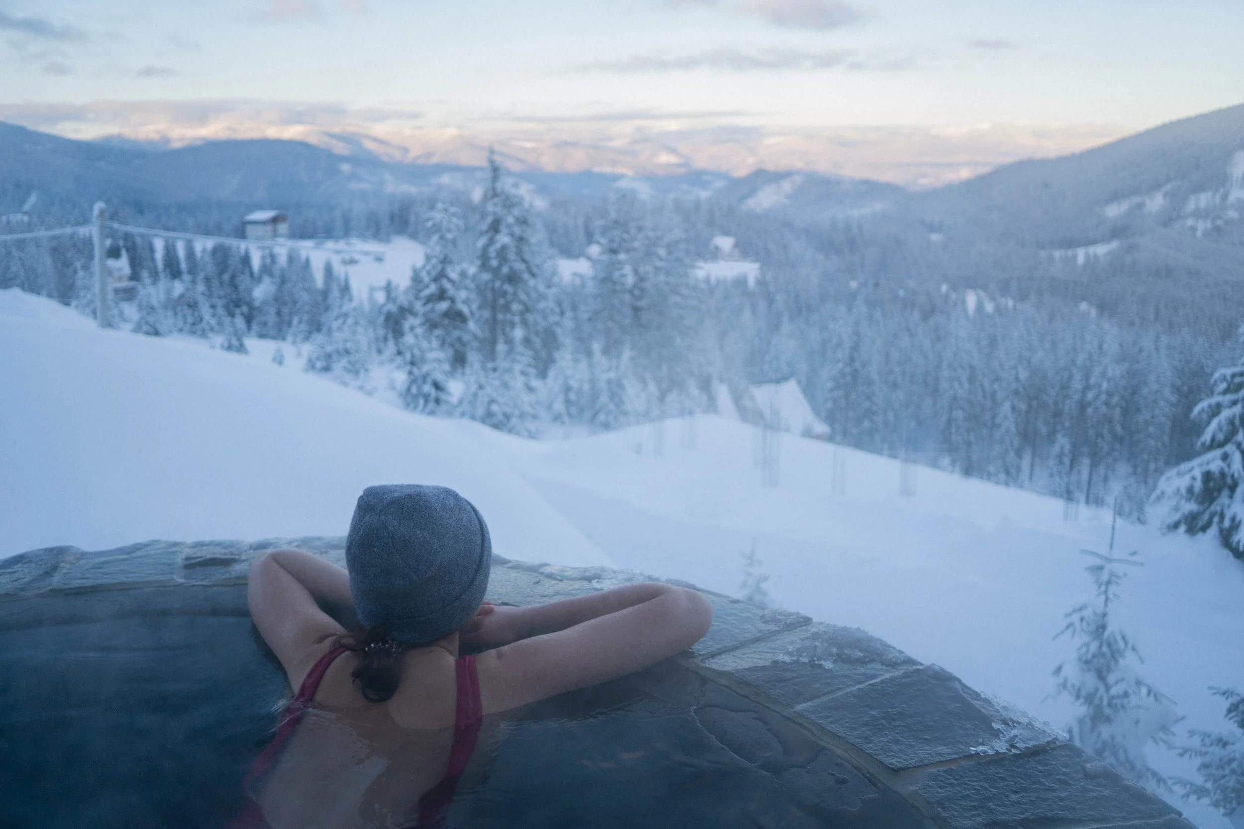 wellnessretreat in Italy lady in hot tub looking at the snowy mountains wearing a wooly hat and red swimming costume