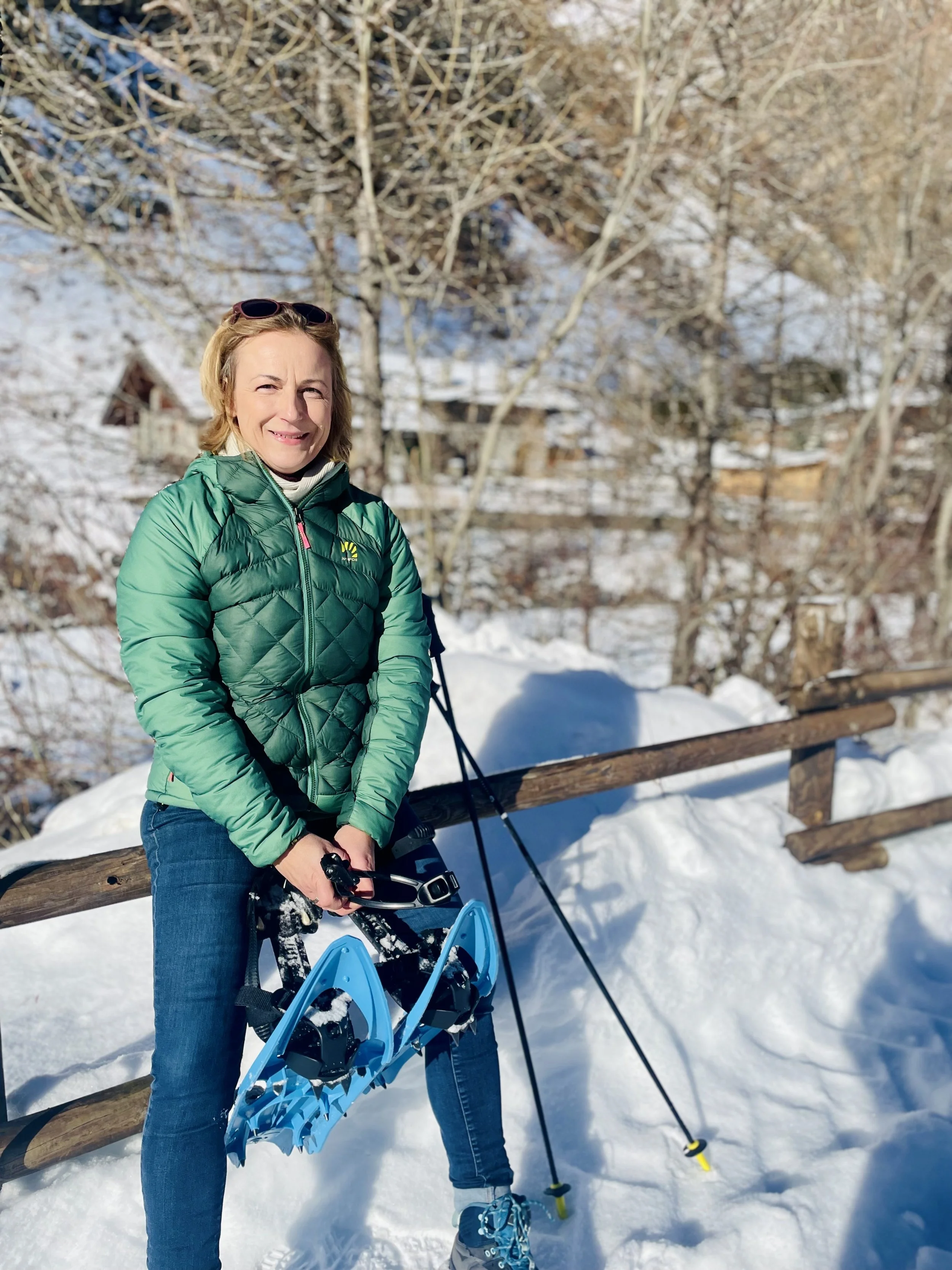 women in snow in the mountains with snowshoes in her hands, wearing jeans and green jacket in Aosta Valley Italy