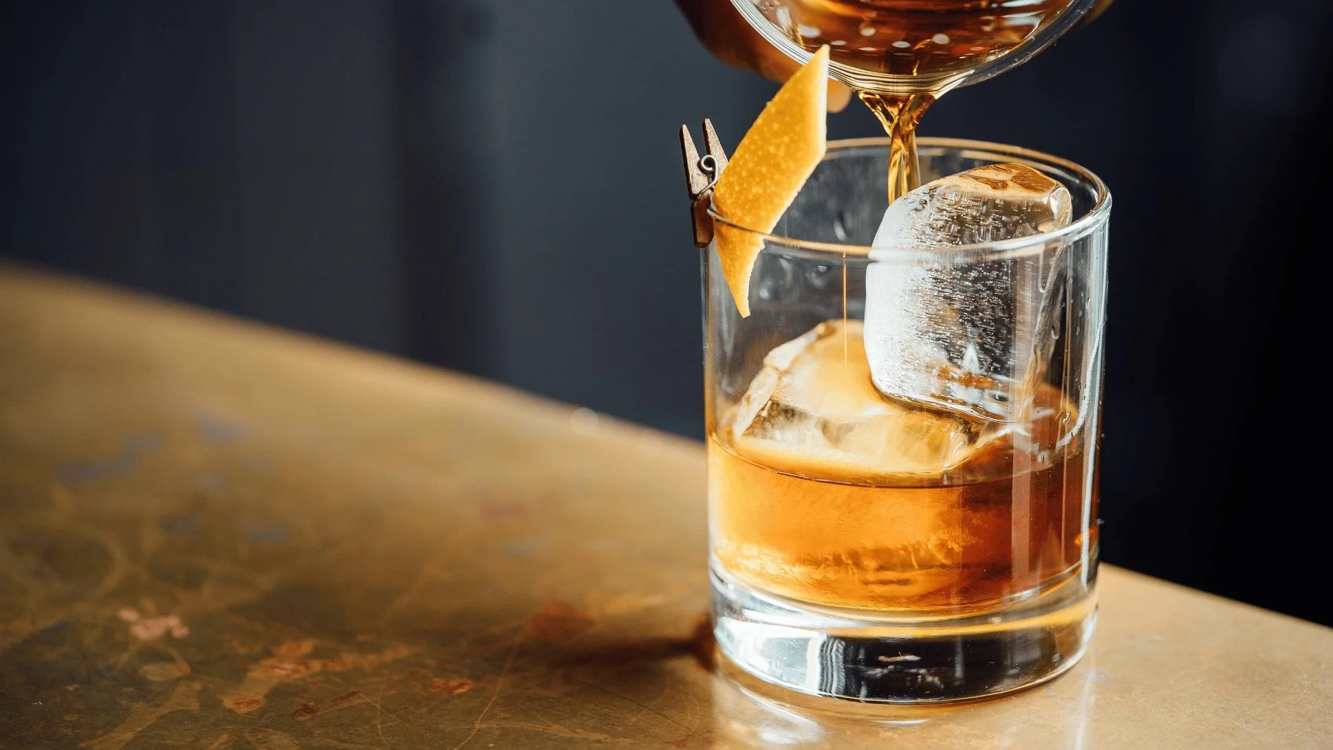 An Old Fashioned cocktail being poured into a glass on a bar