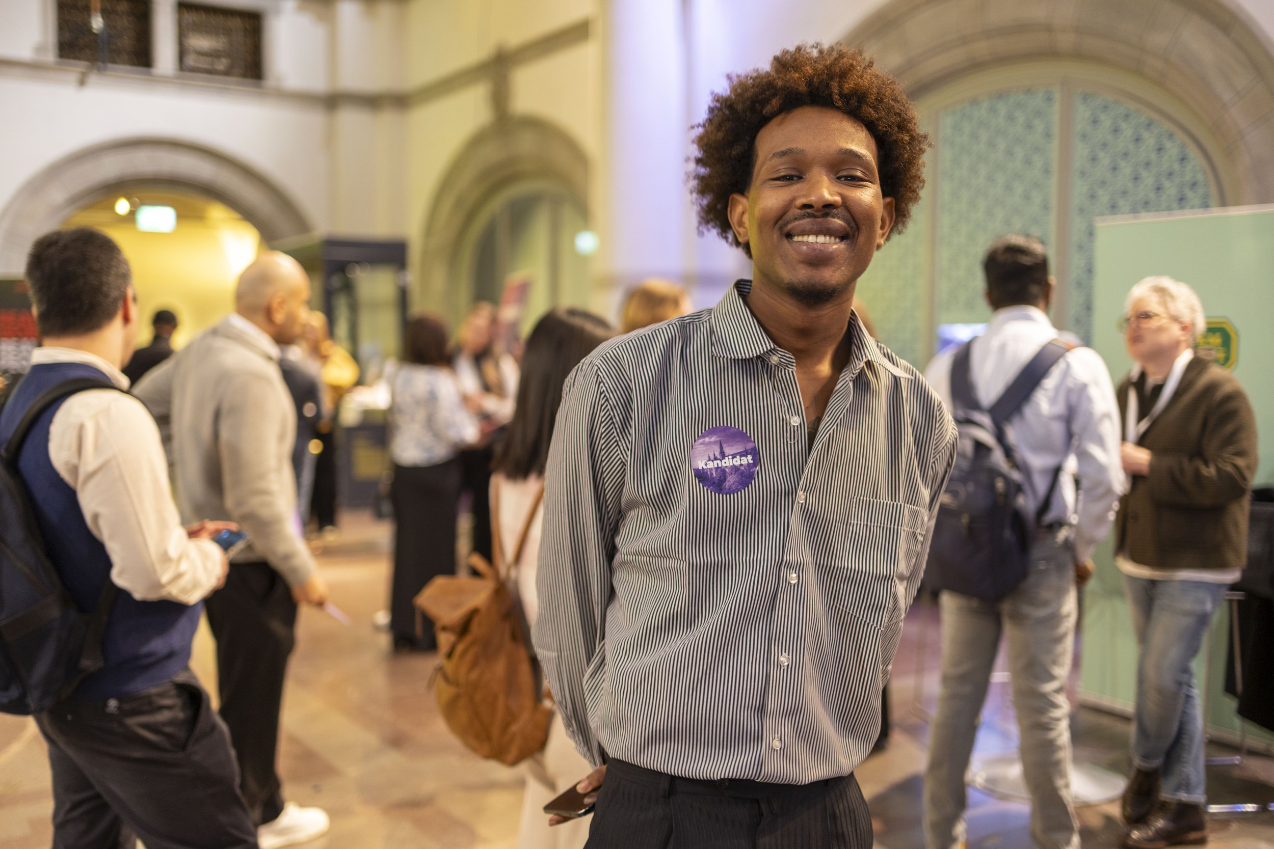 Leende man med brunt hår och bruna ögon, står fram för förbipasserande människor