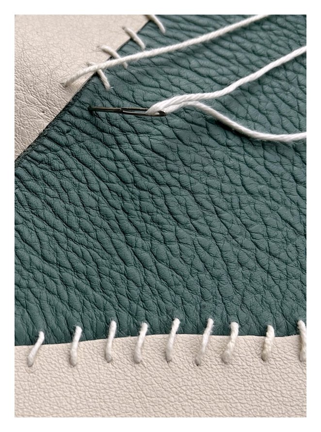 Close-up of a needle stitching green and white eco-leather with white thread