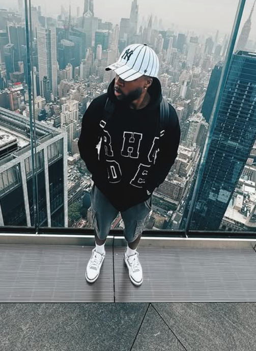 Person mit Kapuzenpullover und Baseballkappe auf einem Hochhaus mit Blick auf die Skyline von New York City.