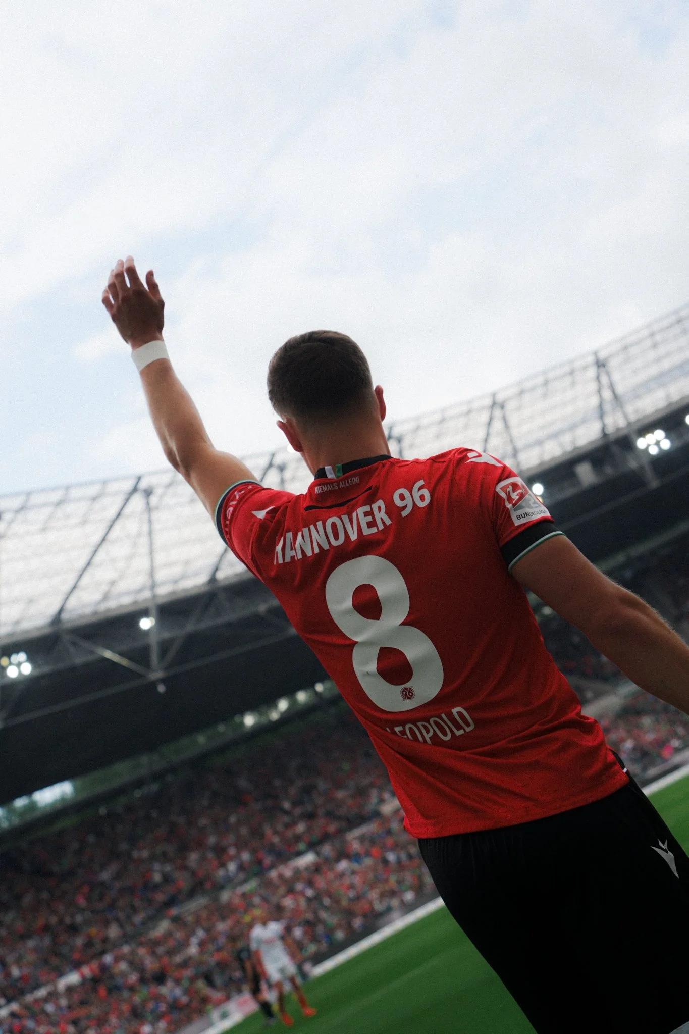 Enzo Leopold im Hannover 96 Trikot mit der Nummer 8 hebt die Hand im Stadion.