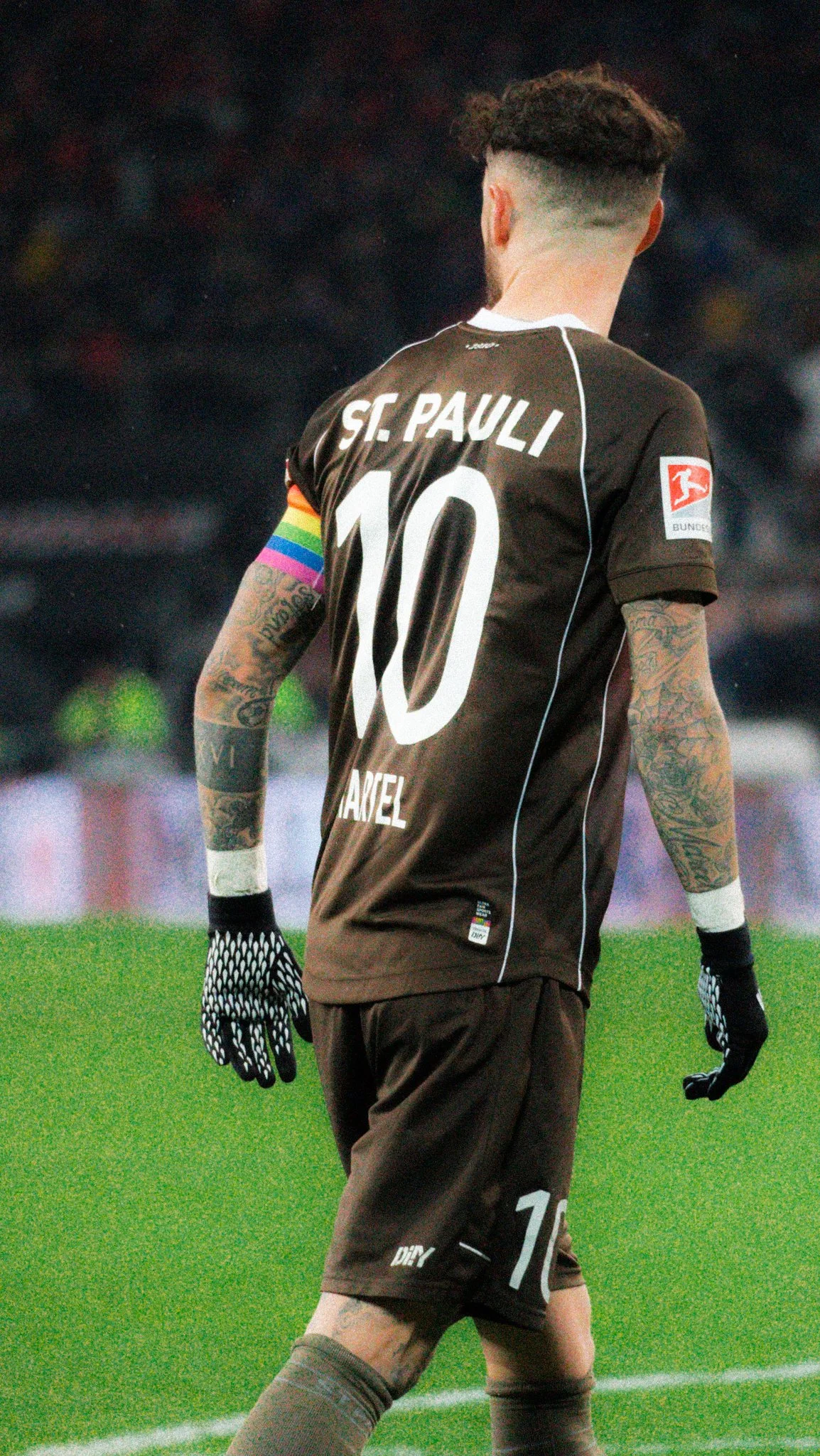 Fußballspieler in St. Pauli Trikot mit Nummer 10 und Regenbogen-Armbinde, von hinten gesehen.