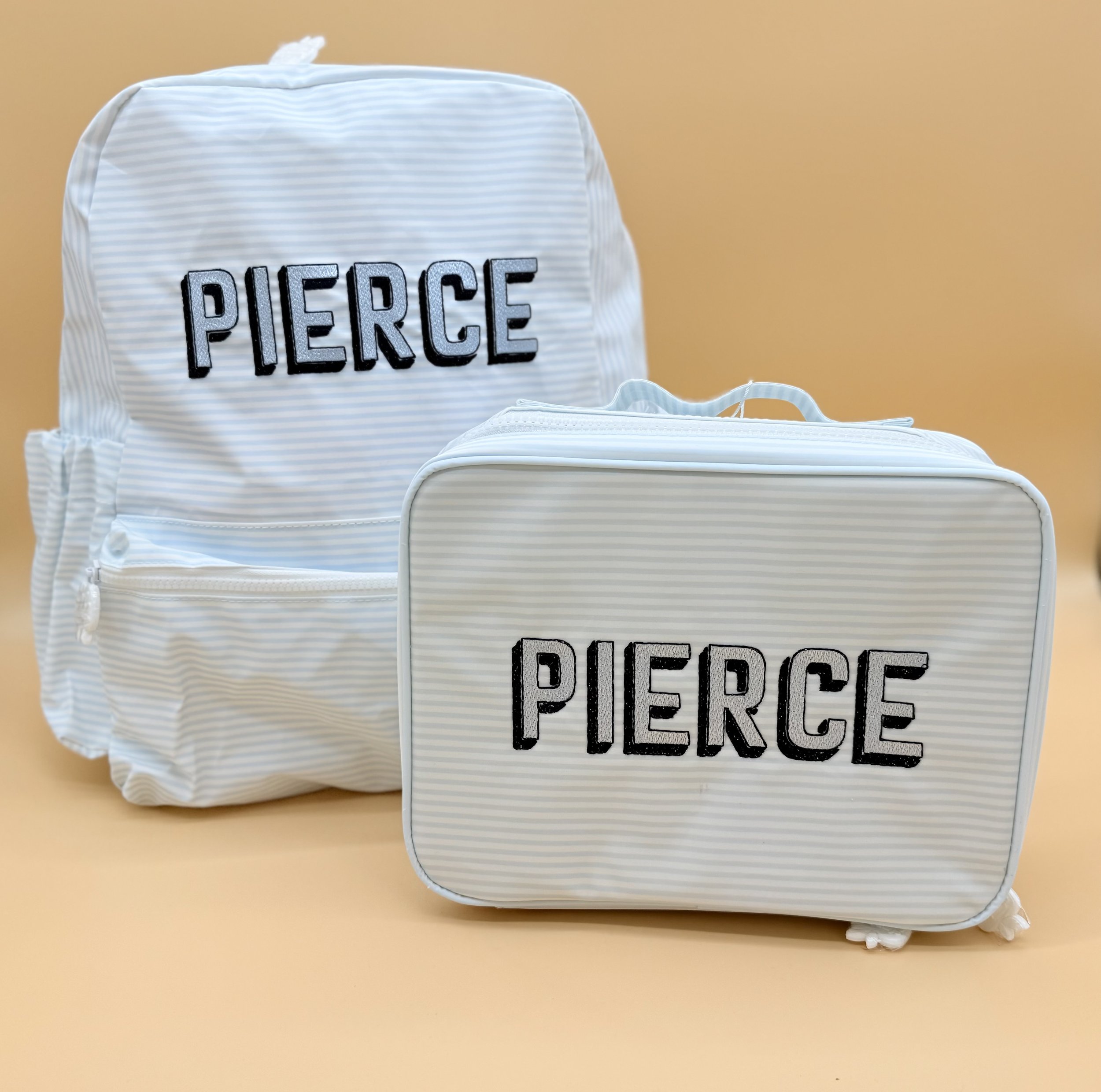 White striped backpack and matching lunch bag personalized with the name Pierce in black embroidery.