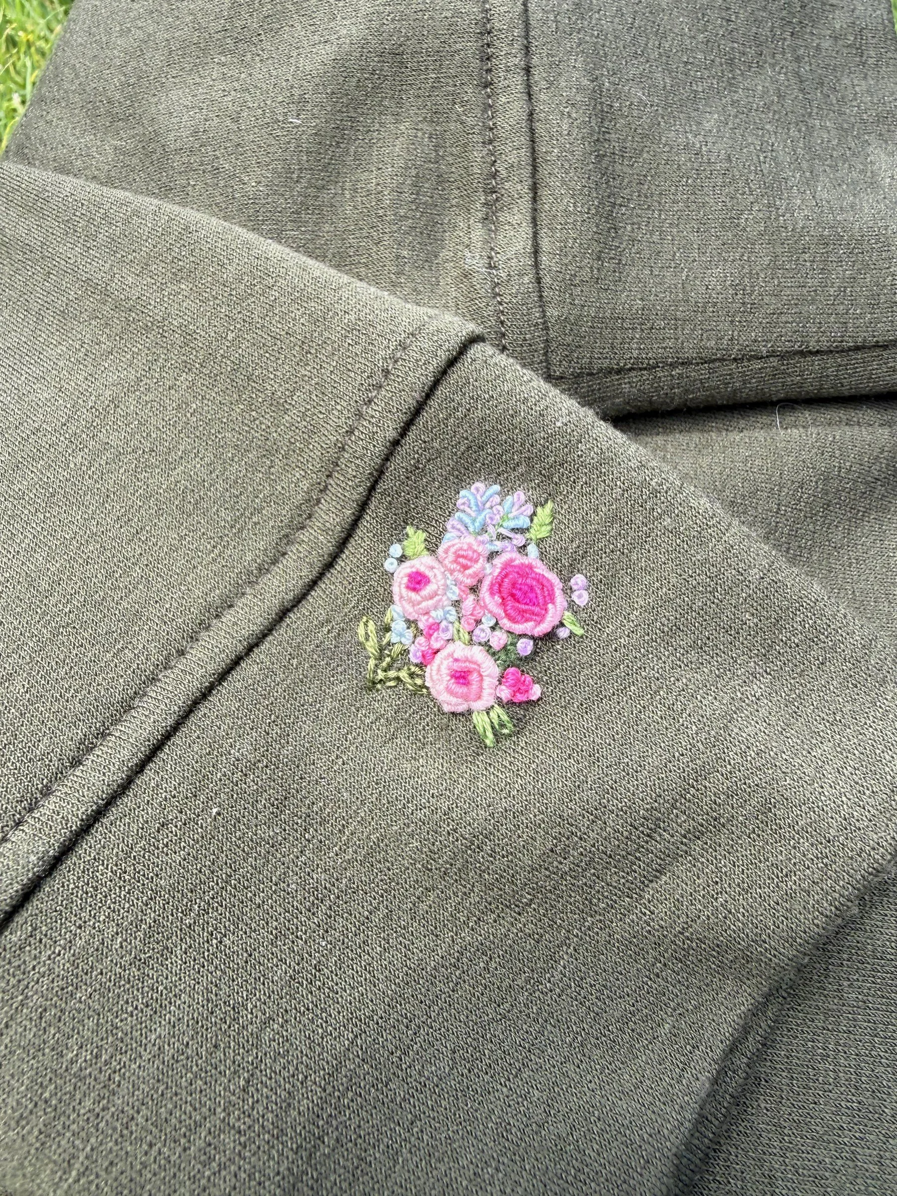 A tiny pink floral bouquet hand embroidered on an olive sweatshirt cuff.