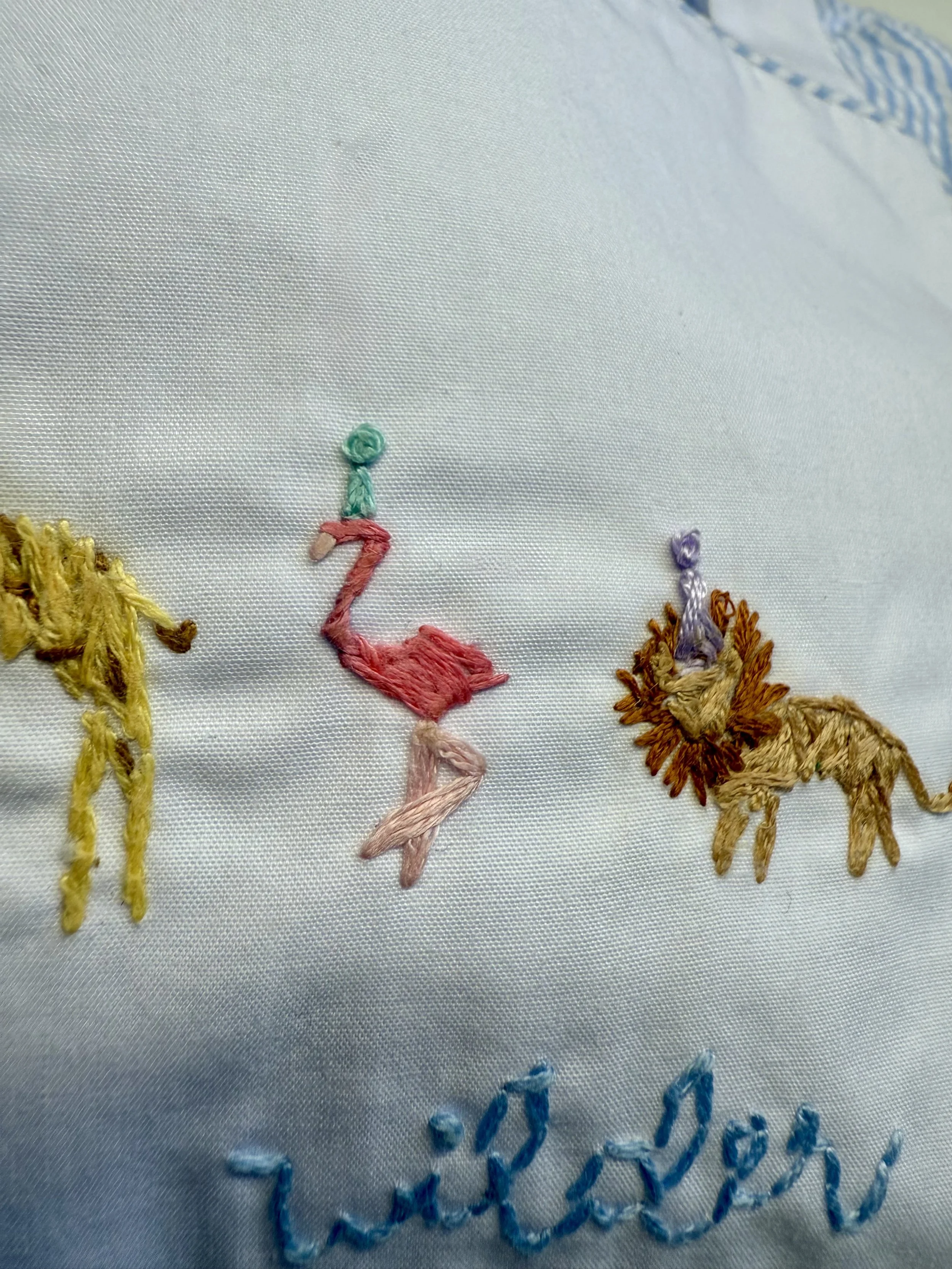 Embroidery of a pink flamingo, a yellow giraffe, and a lion with a purple mane on white fabric.