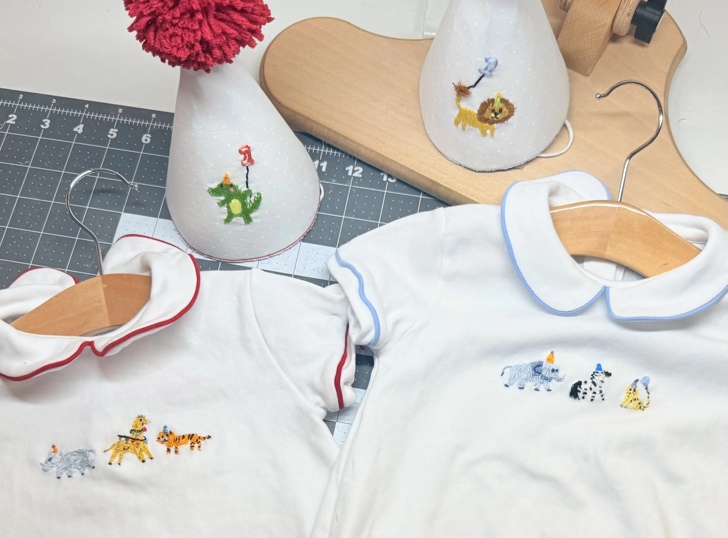 White children’s outfits and matching party hats decorated with embroidered animal motifs.