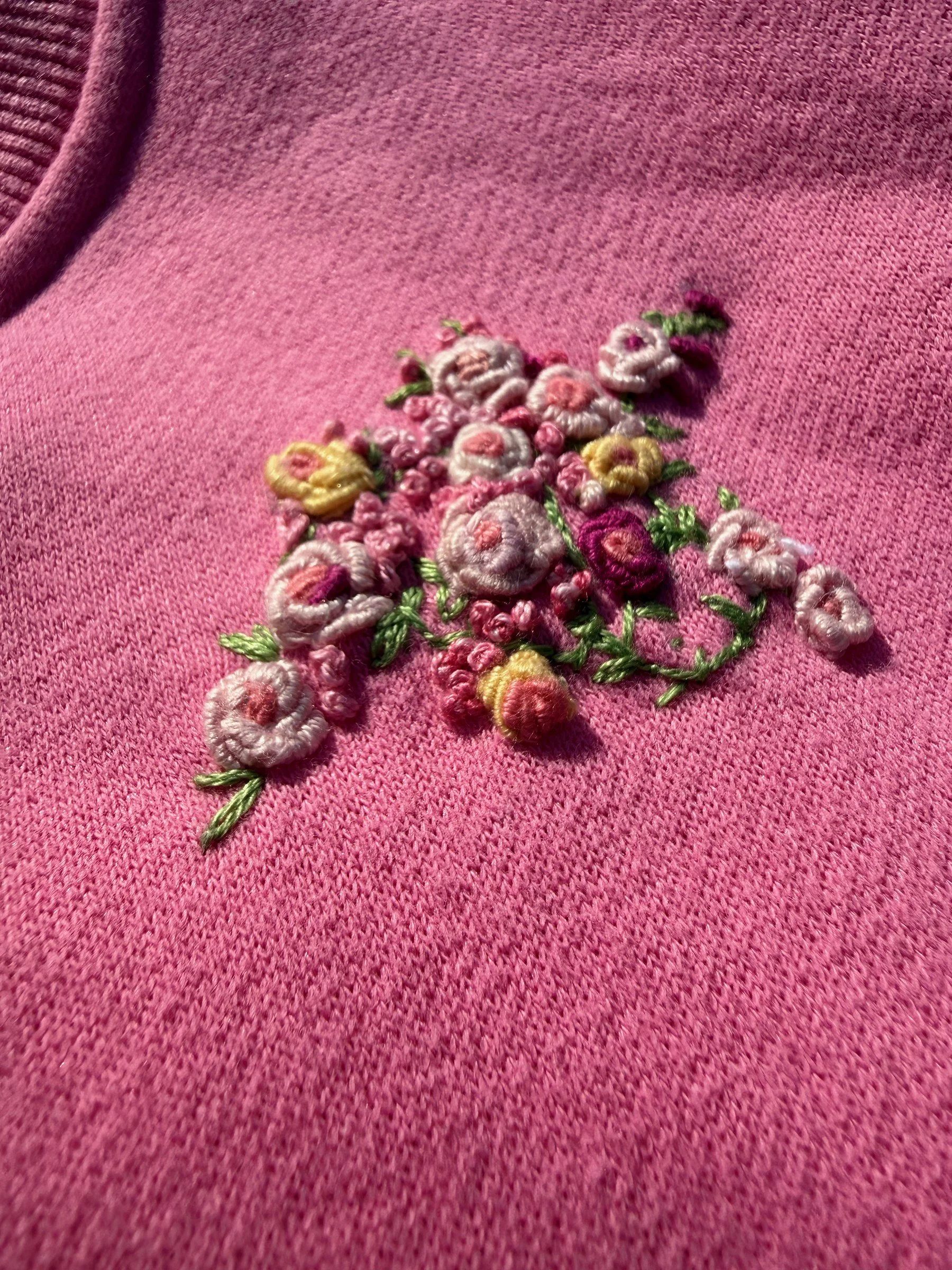 Raised roses and green leaves hand embroidered on a pink sweatshirt.