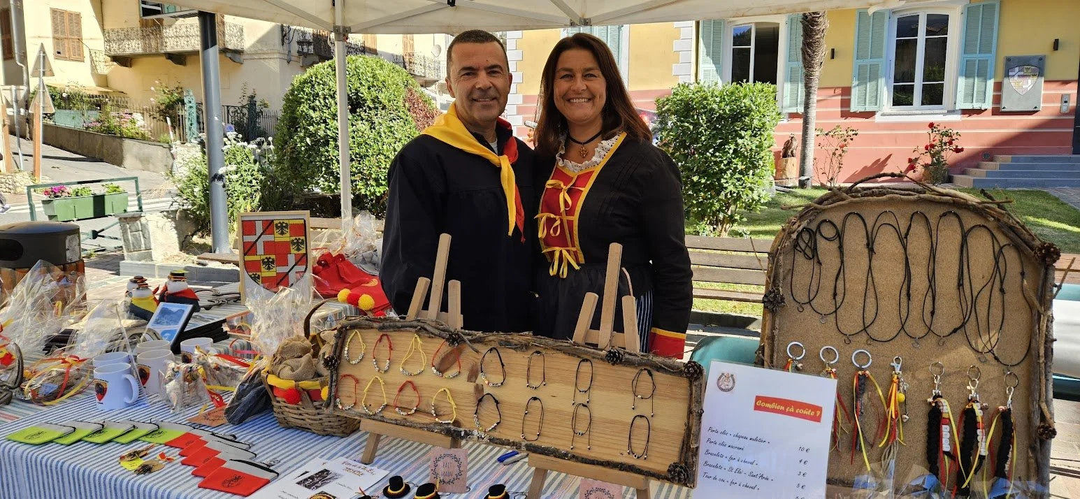 Deux personnes souriantes en tenues traditionnelles près d'un stand avec des bijoux artisanaux et des articles décoratifs.
