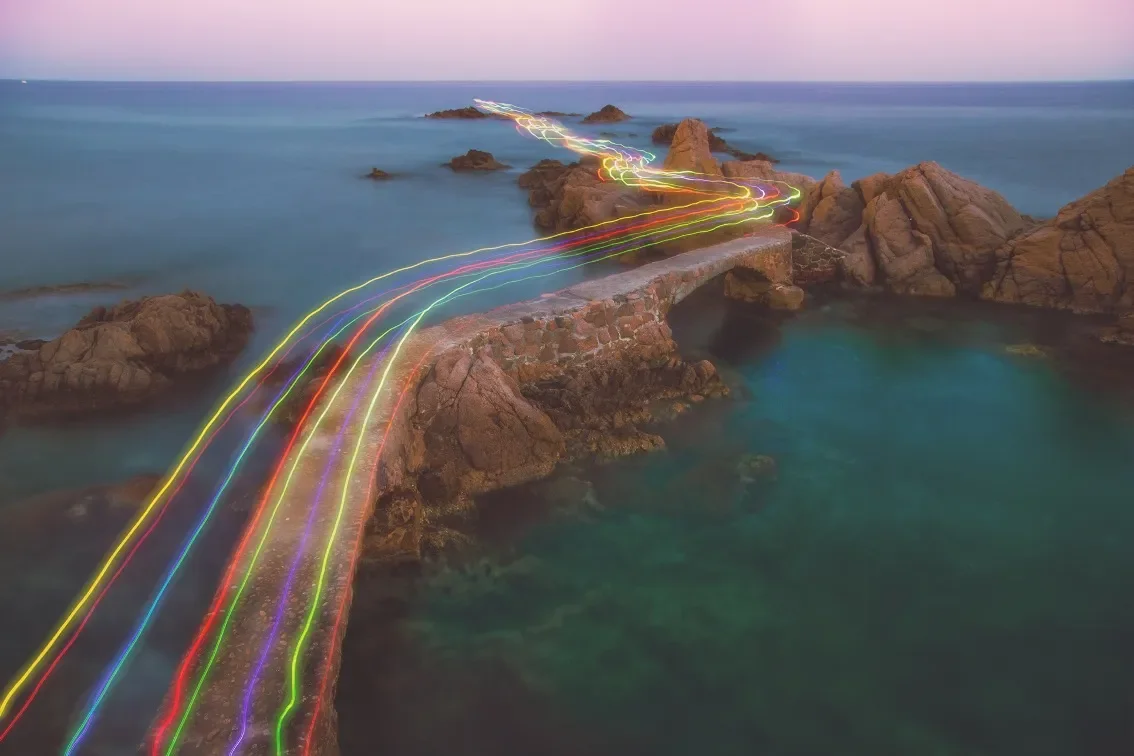 Light trails crossing a stone bridge over the sea, symbolizing Metheus Consultancy’s growth and scale consulting services that help businesses accelerate expansion and reach new heights.