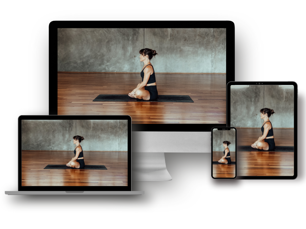 Multiple electronic devices displaying a woman in a yoga pose in a yoga studio with a concrete wall and wooden floor.