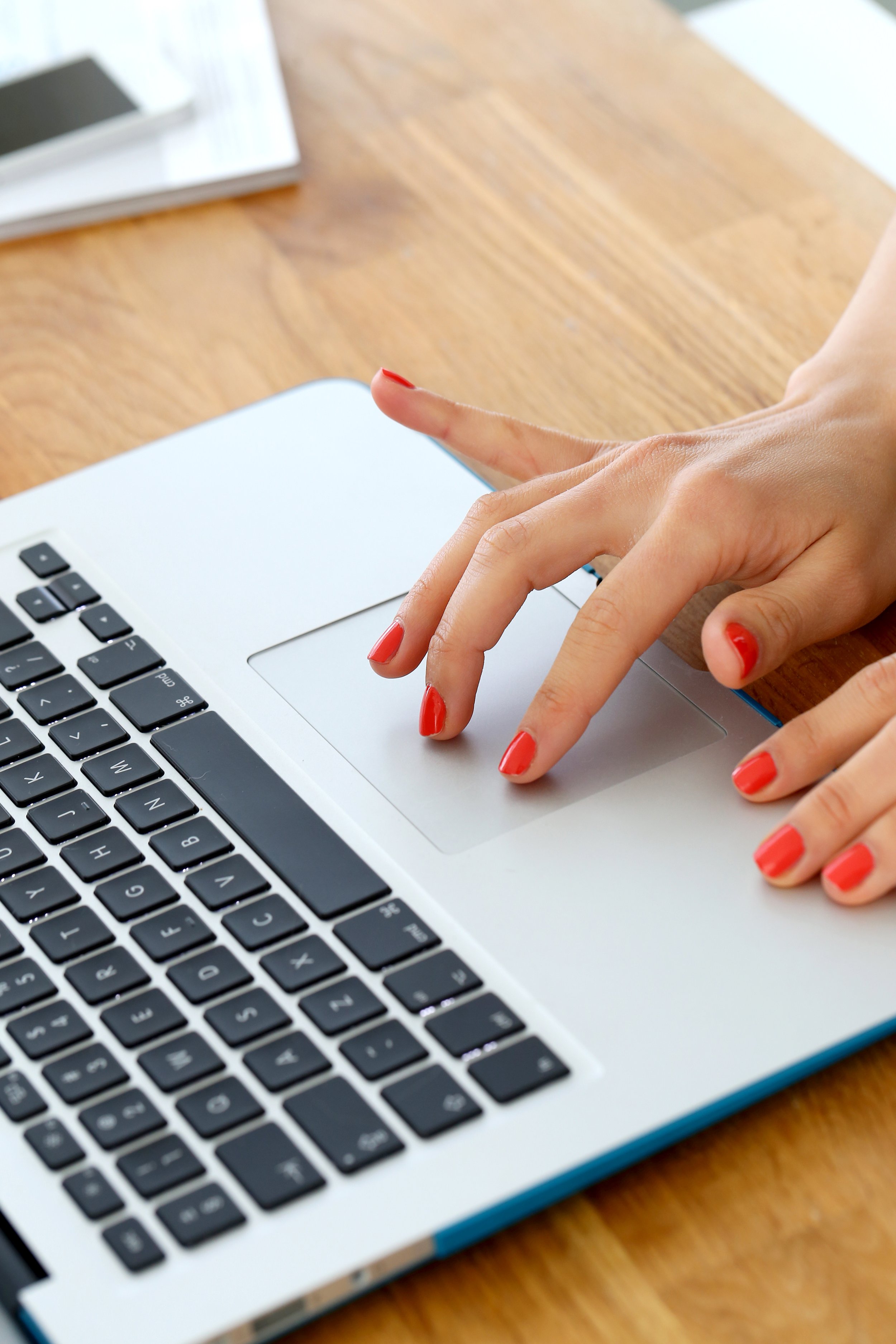 Person using a laptop trackpad while working at a wooden desk.