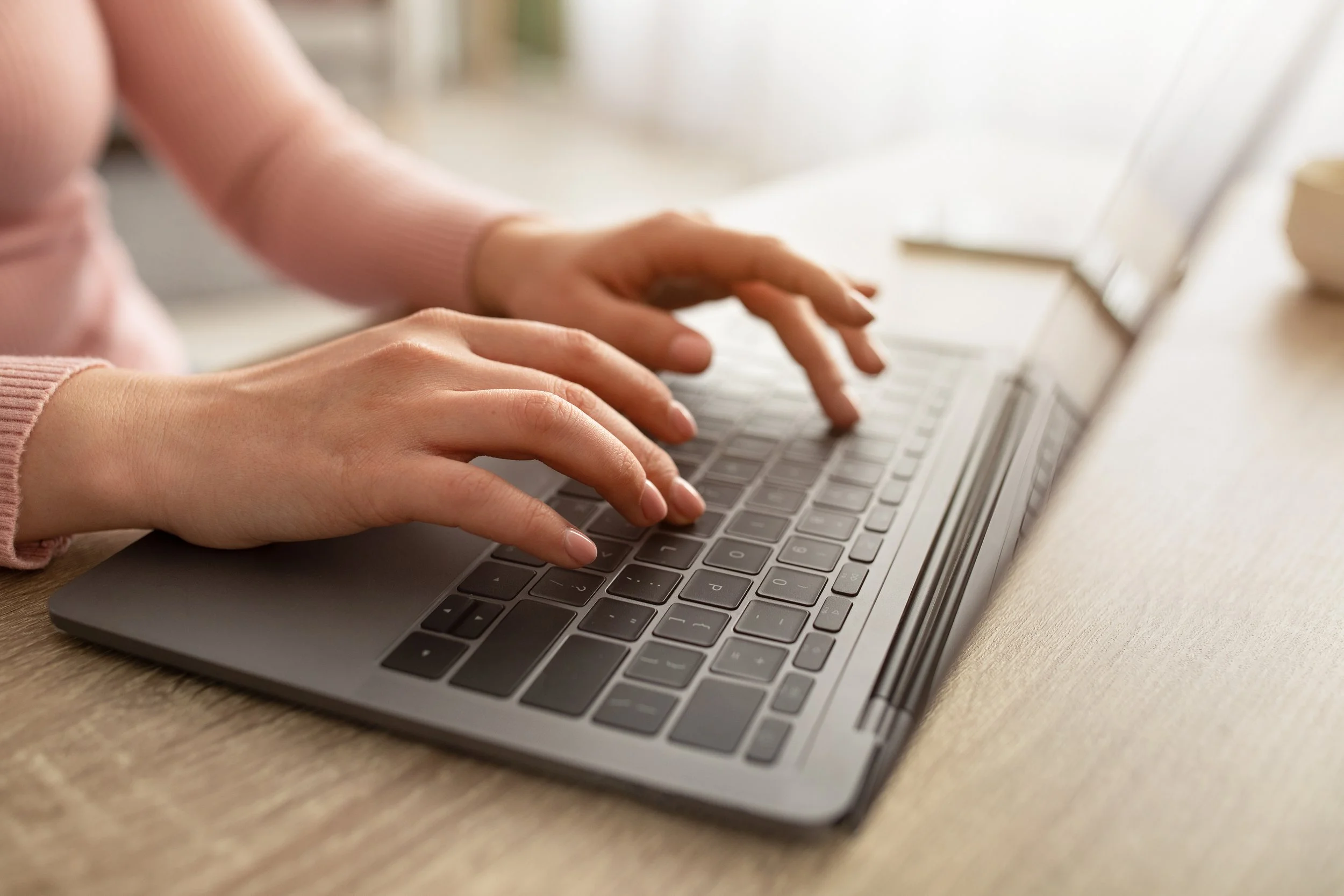Close-up of hands typing on a silver laptop keyboard placed on a wooden surface.