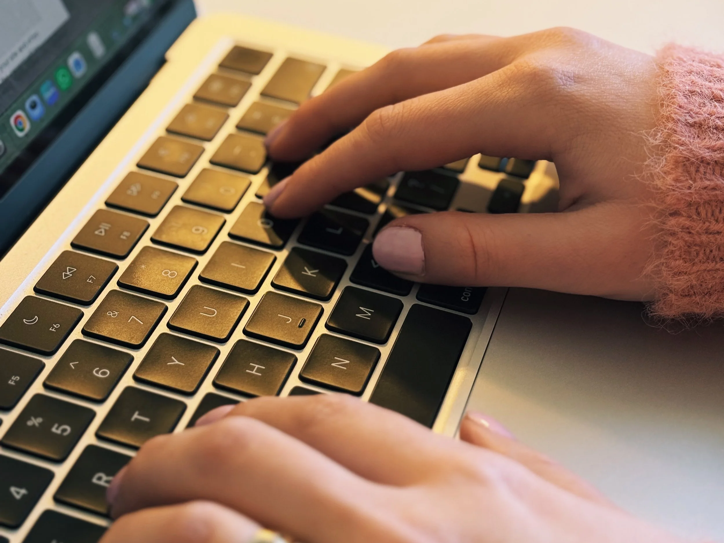 Close-up of hands typing on a laptop keyboard in a home office setting.  Work-focused: