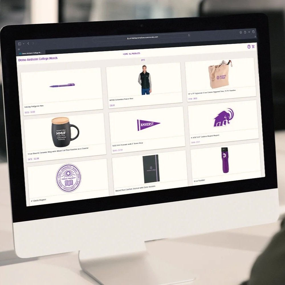 Computer screen displaying a webpage with Amherst College merchandise including a pen, a jacket, a tote bag, a mug, a pennant, a house icon, a journal, and a water bottle.