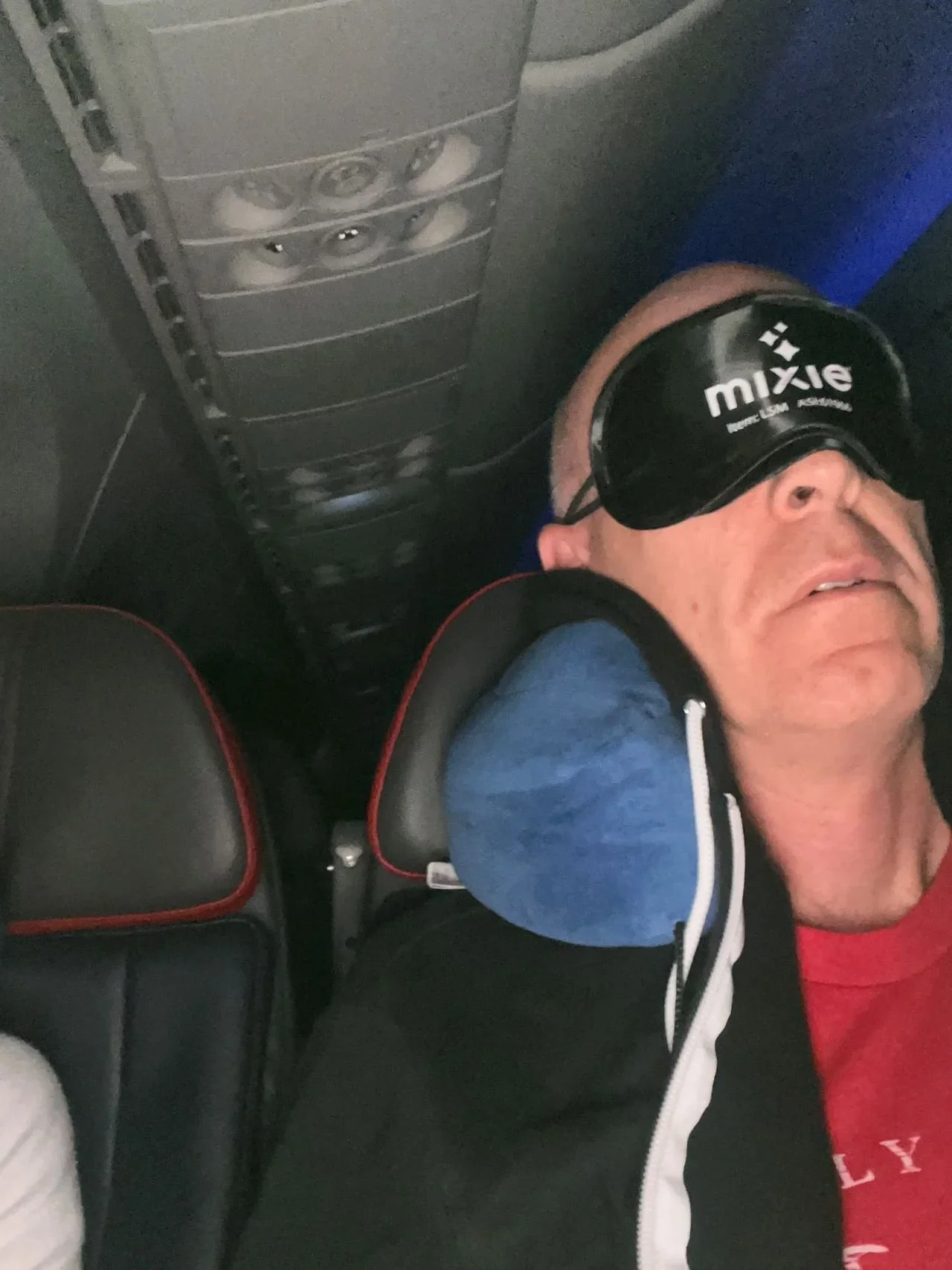 “Sleep In Kit” on an airplane seat: a lip moisturizer, fabric spray, sleep mask, and earplugs. The photo captures the kit in action during a flight, demonstrating its practicality as a travel gift.