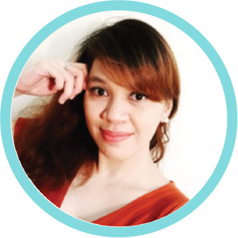 A woman with reddish-brown hair smiling and posing for the camera, wearing an orange top.