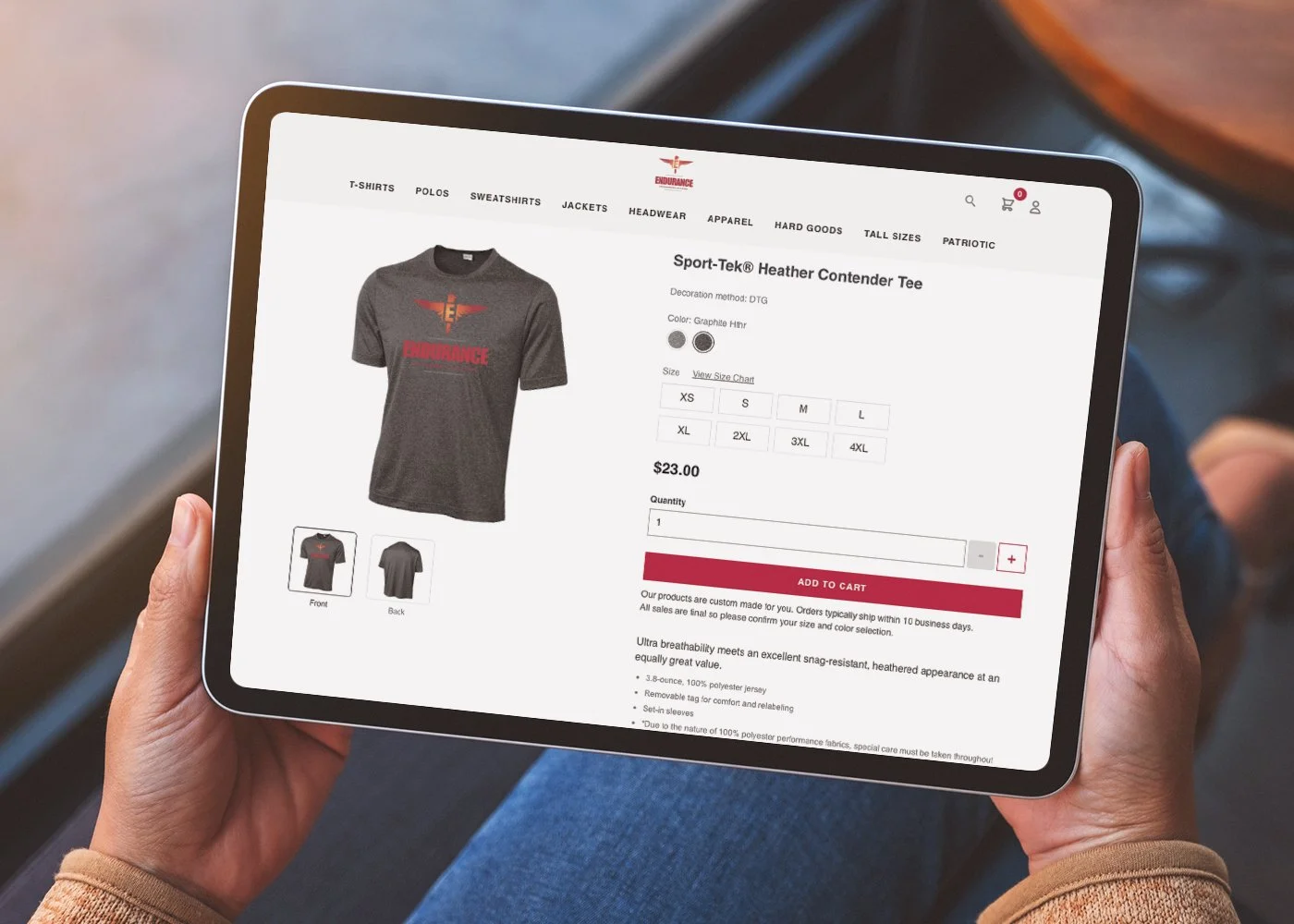 Person holding a tablet displaying an online store page for a gray Heather Contender Tee with red and black logo, showing options for size and color.