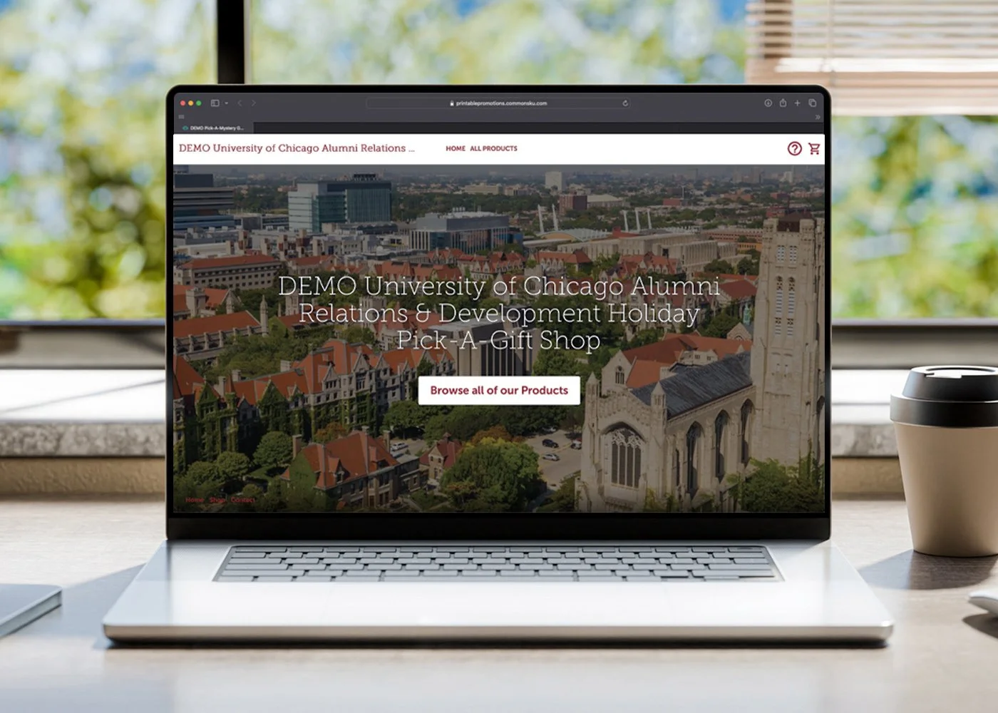Laptop on a desk with a website for the University of Chicago Alumni Relations displayed, showing a cityscape with buildings and a church in the background.