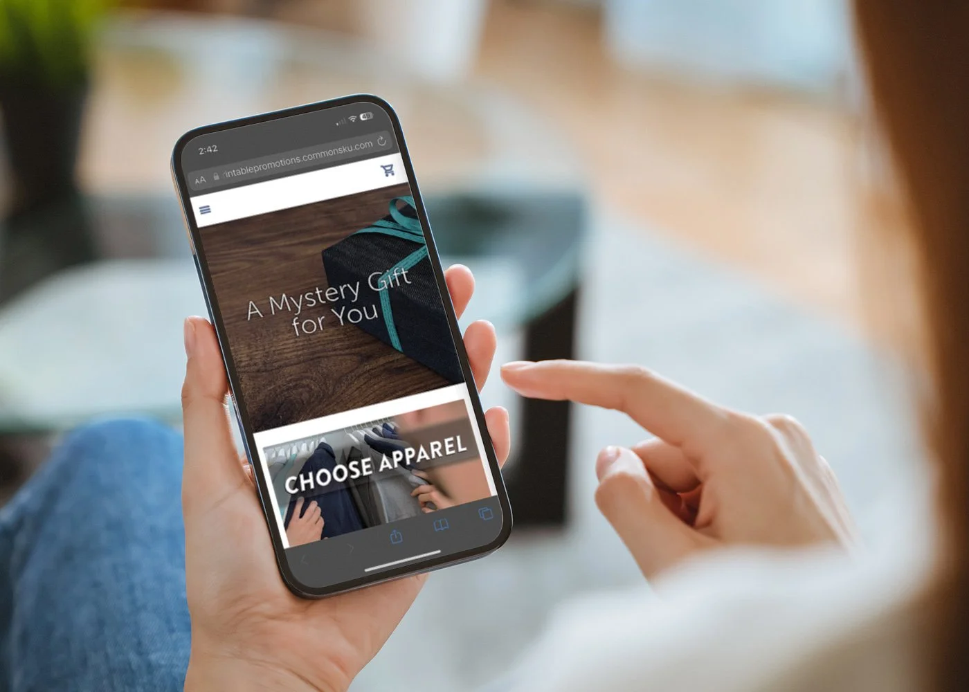 Person holding a smartphone displaying an online shopping website for apparel, with a gift box image and the words "A Mystery Gift for You" and "CHOOSE APPAREL"