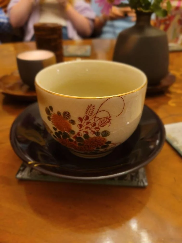 A decorative teacup with a floral pattern on a black saucer, placed on a wooden table.
