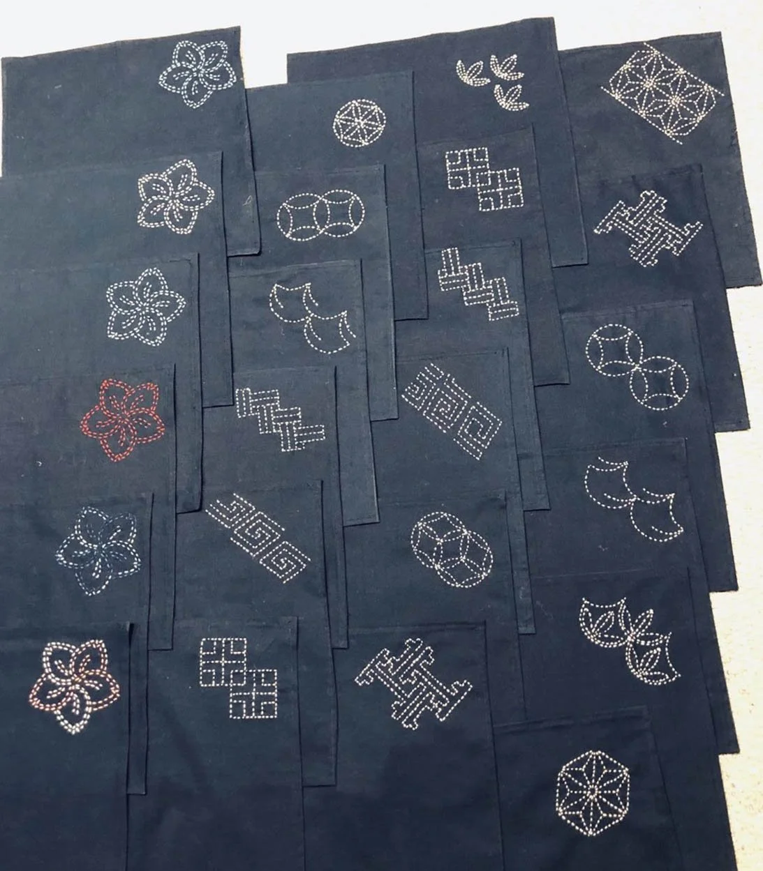 Multiple black fabric pieces with white and red geometric and floral patterns sewn into them, arranged in overlapping layers.