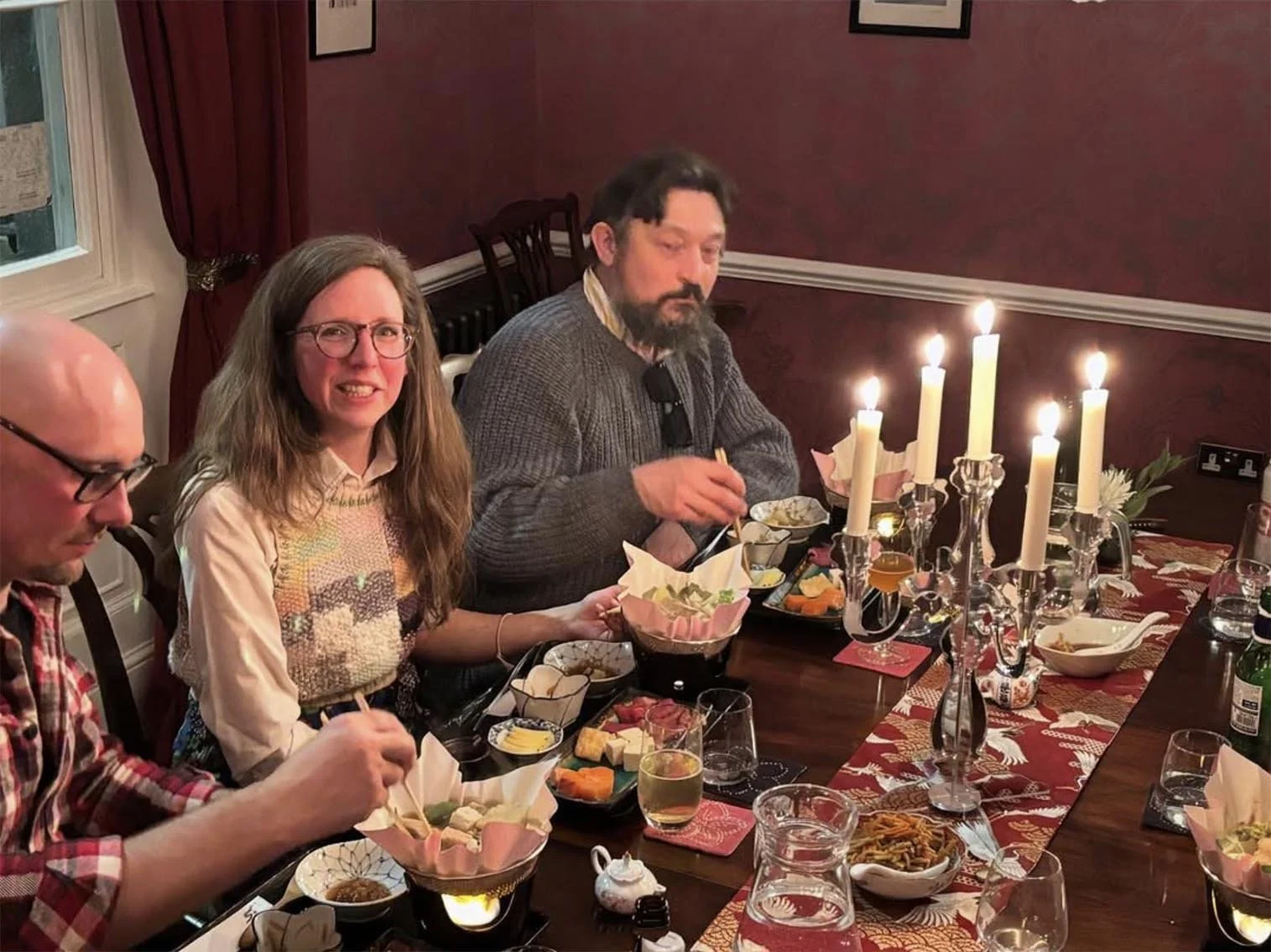 People having a dinner gathering at a festive holiday meal with lit candles, various dishes, and food on the table.