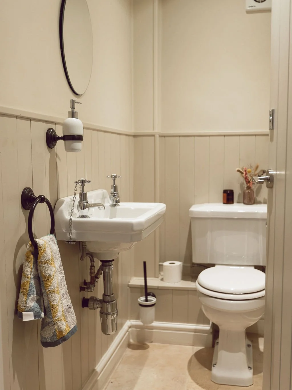 Small bathroom with wall-mounted sink, toilet, mirror, and minimal decor; beige wall paneling and floor.