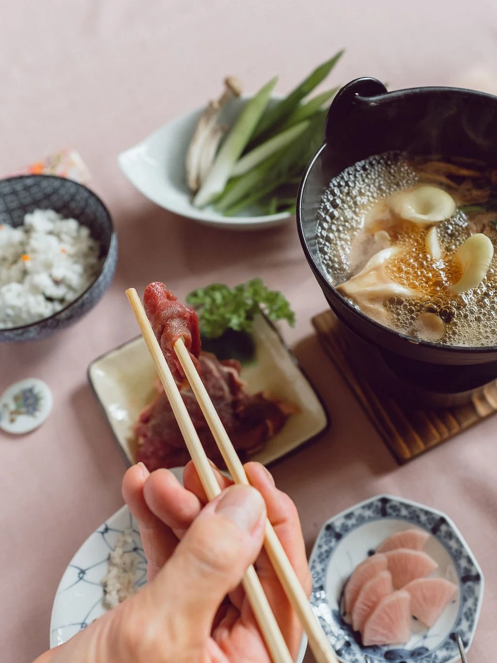Japanese hot pot meal with vegetables, thinly sliced meat, rice, and sashimi.
