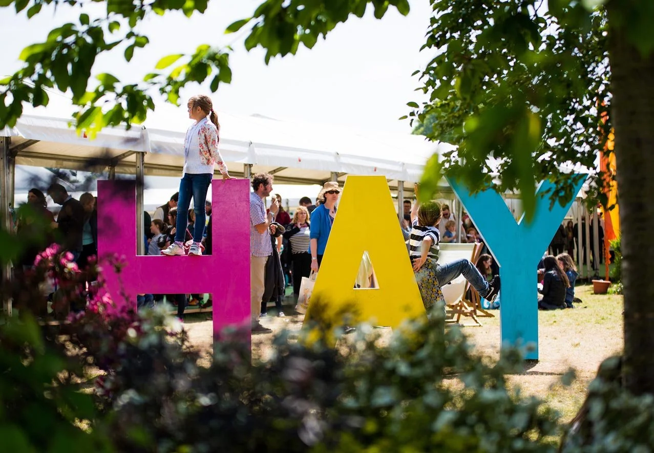 People gathering at an outdoor event behind large colorful letters spelling 'HAY'.