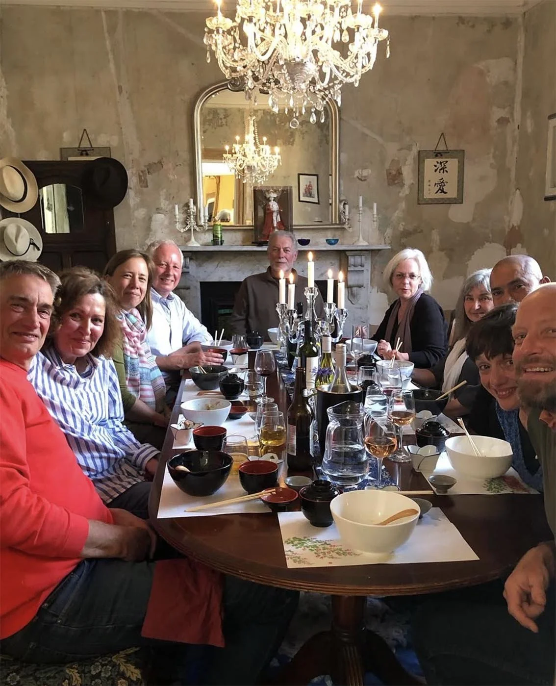 Group of ten people sitting around a dining table in a decorated dining room with a chandelier and a large mirror on the wall.