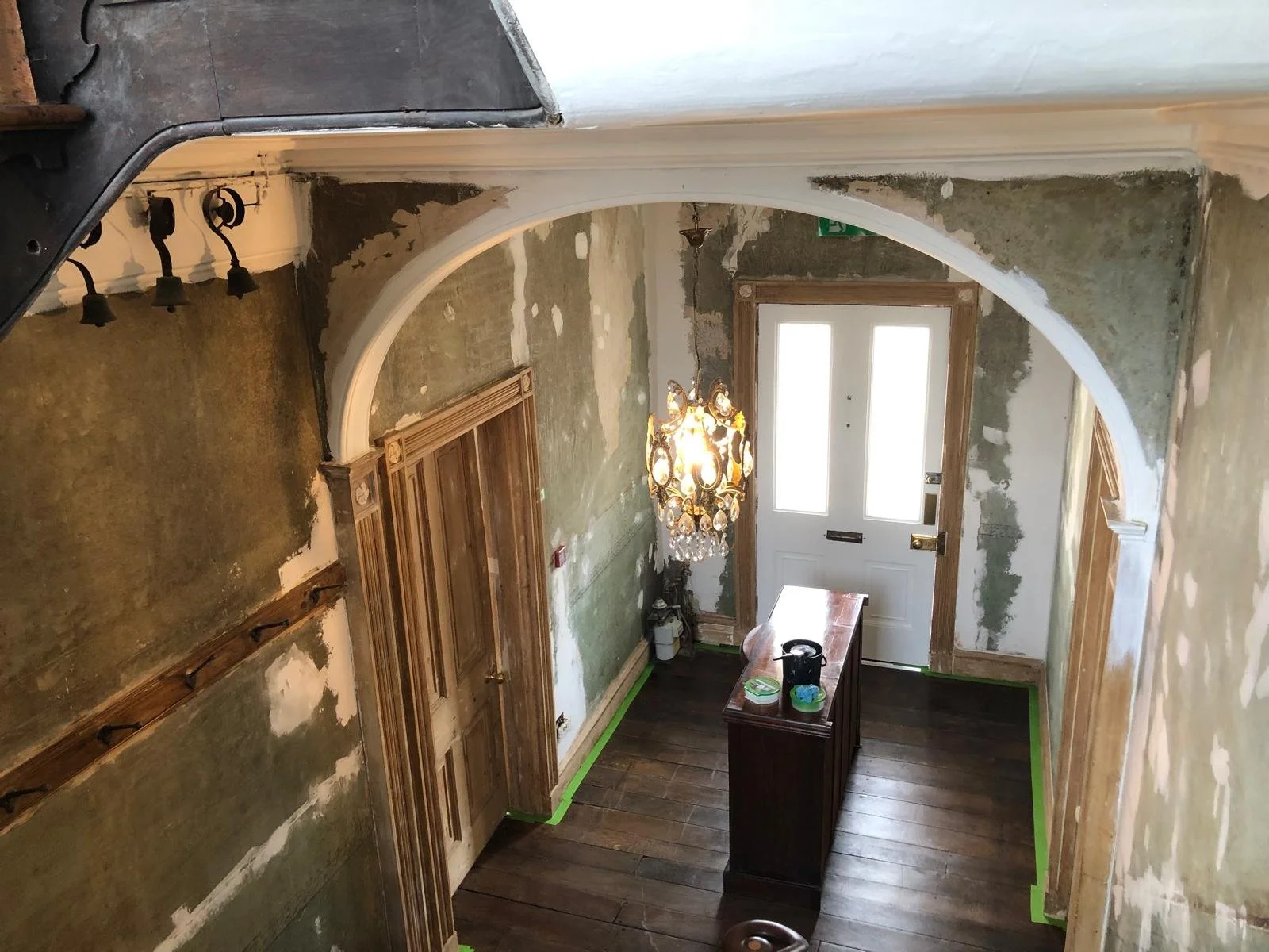View of a foyer with an arched doorway, wooden trim, a chandelier, and an entry door, during renovation or painting.