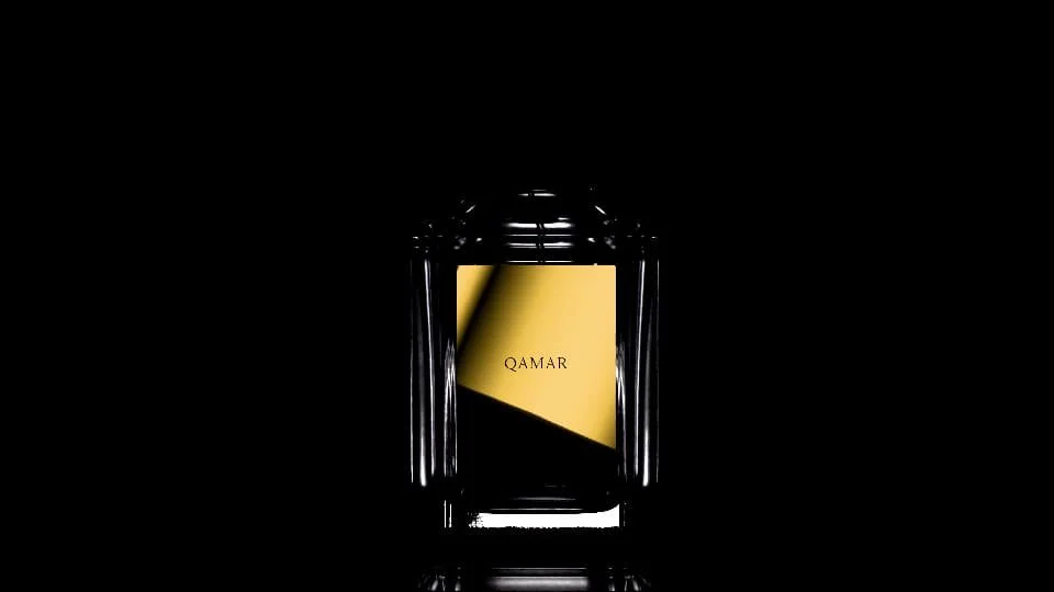 A black perfume bottle with a gold label that reads QAMAR, set against a black background.
