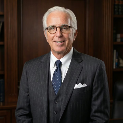 Man wearing a gray plaid suit and white shirt, smiling, with a pocket square.