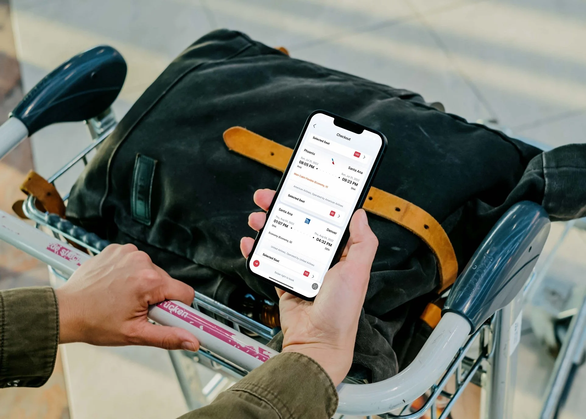 Person holding smartphone with airline app open, next to luggage on airport trolley.