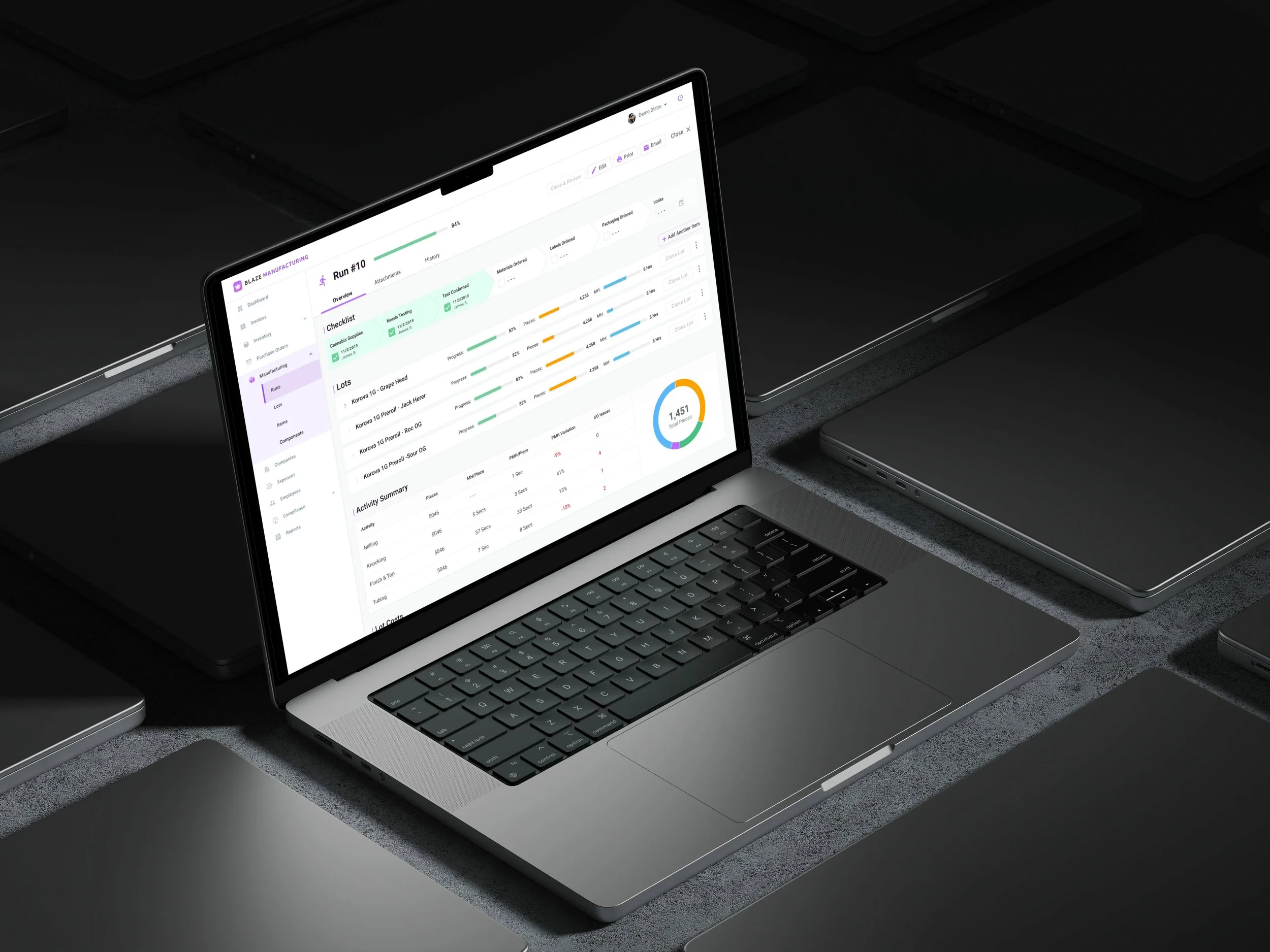 Laptop displaying data management dashboard with charts and tables on screen, surrounded by closed laptops on a dark surface.