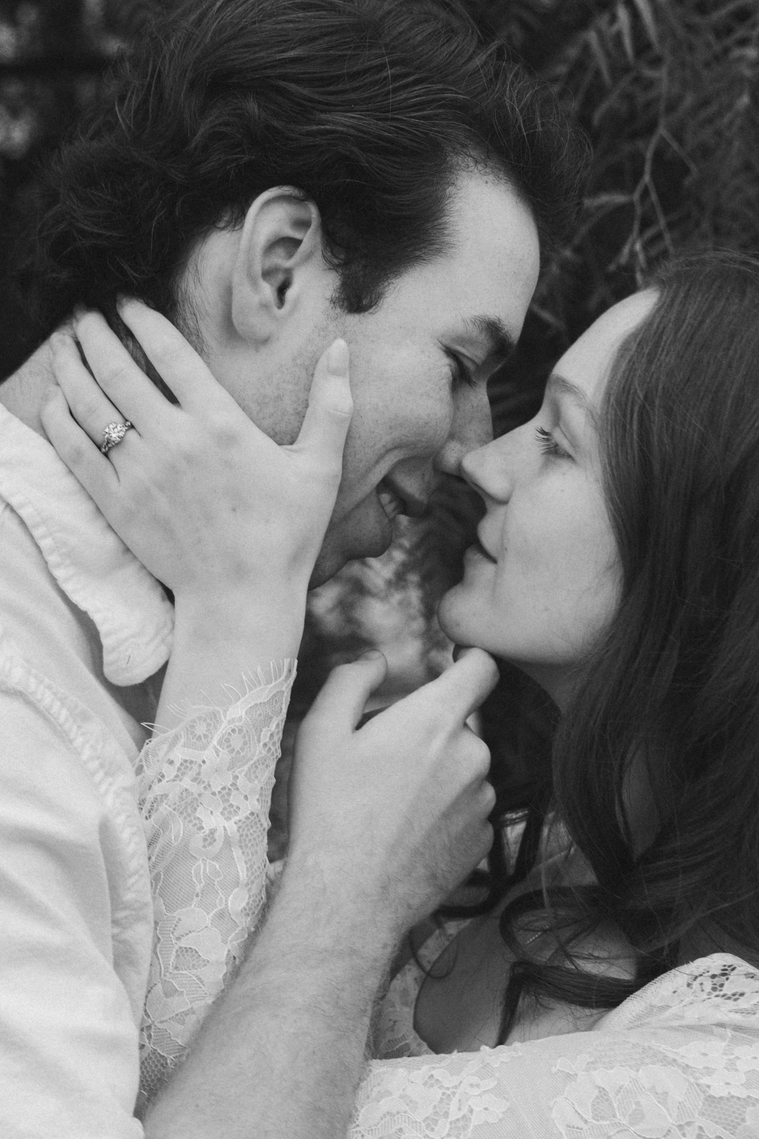 A black and white close-up photo of a couple lying close together, touching foreheads with eyes closed, showing intimate affection.