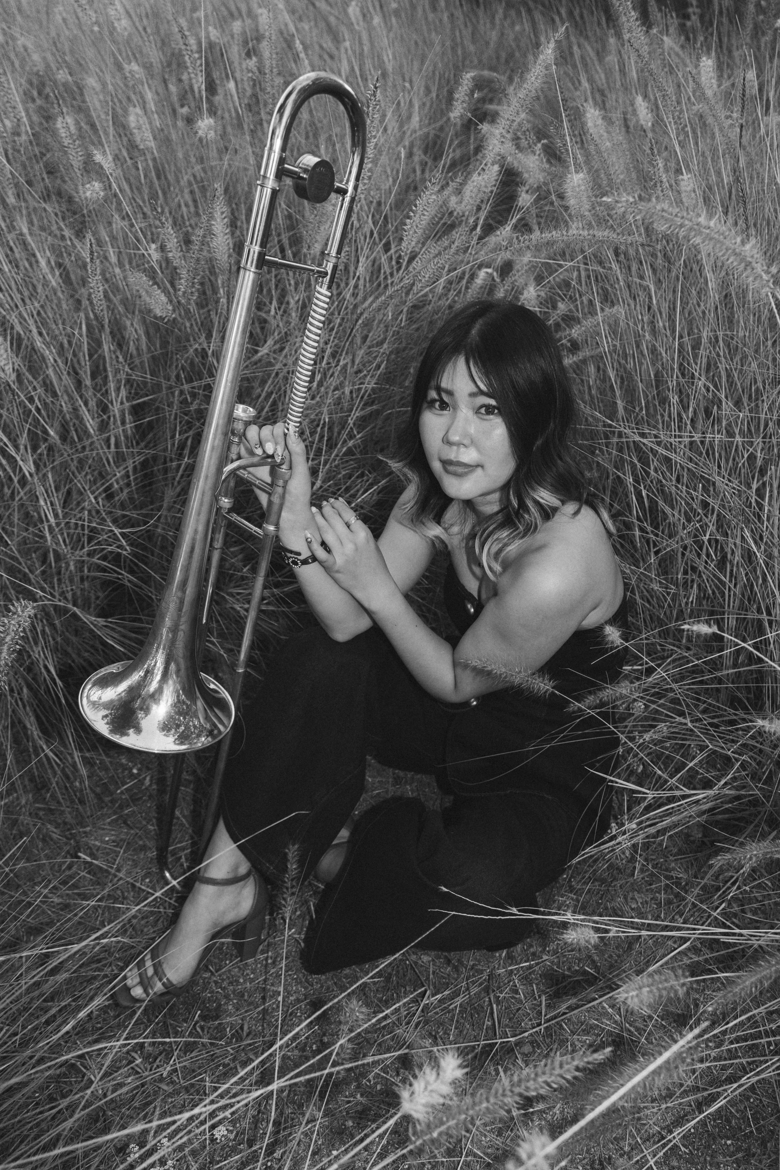 A woman sitting in tall grass holding a trumpet.