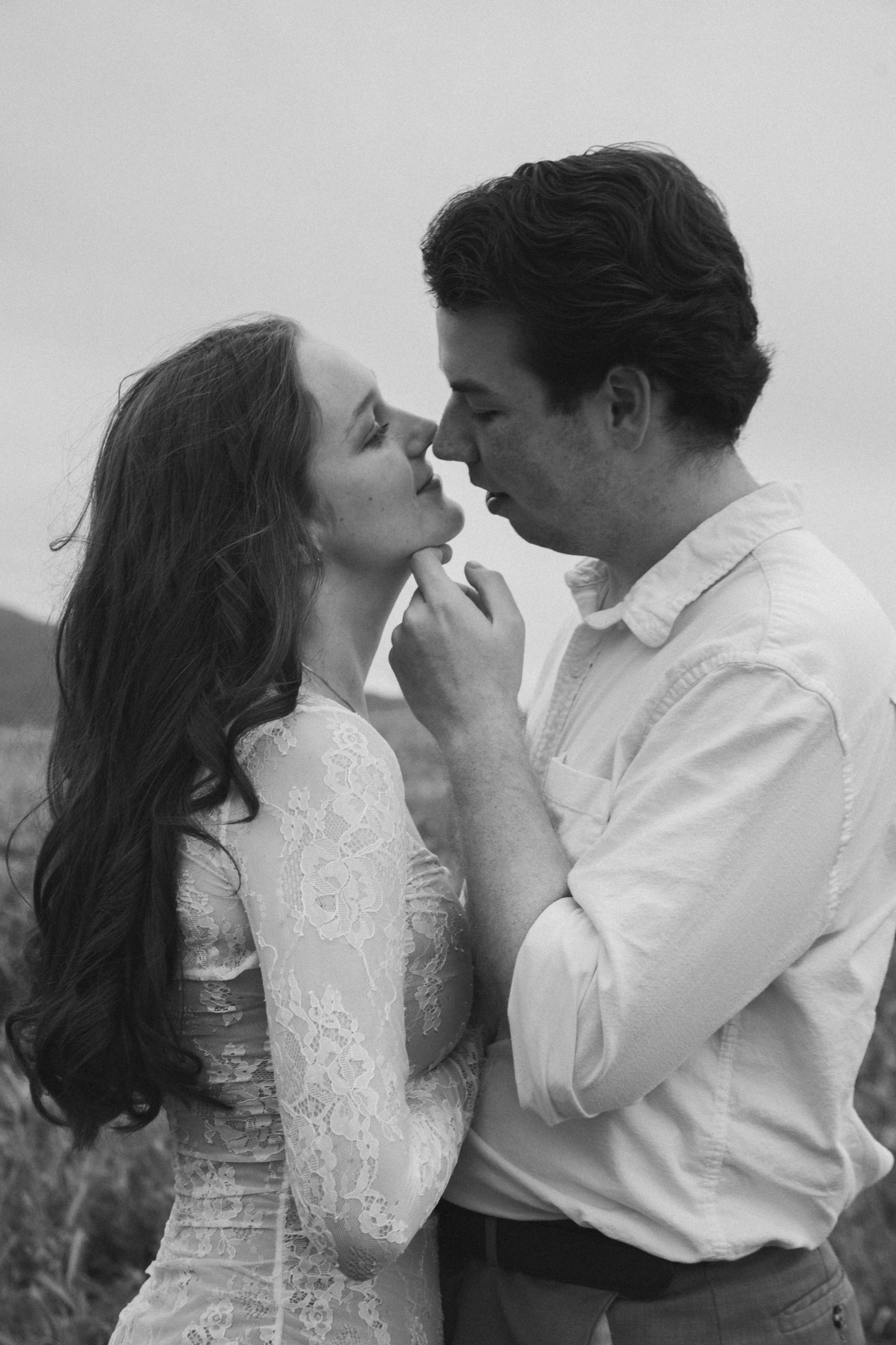 A black-and-white photo of a couple about to kiss, with the woman gently touching the man's face and the man holding her close.