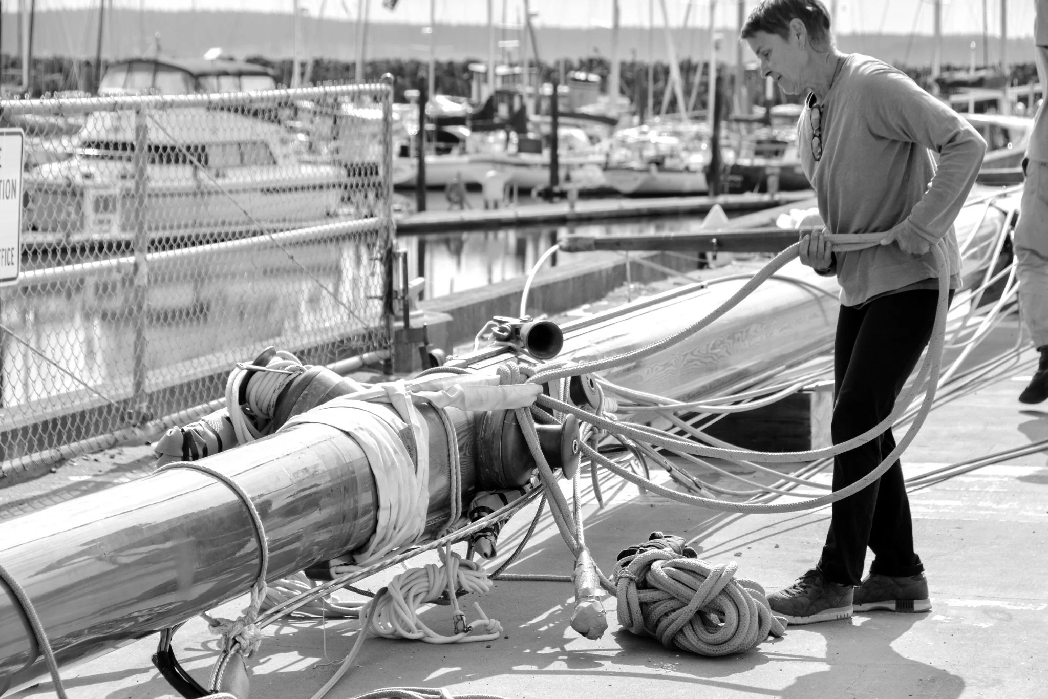 A woman on a dock working on new rigging for a sailboat at the marina in Port Townsend, WA, with docked boats in the background.