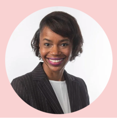 Professional woman with short hair, wearing a black pinstripe blazer and white shirt, smiling against a white background with a pink circular border.
